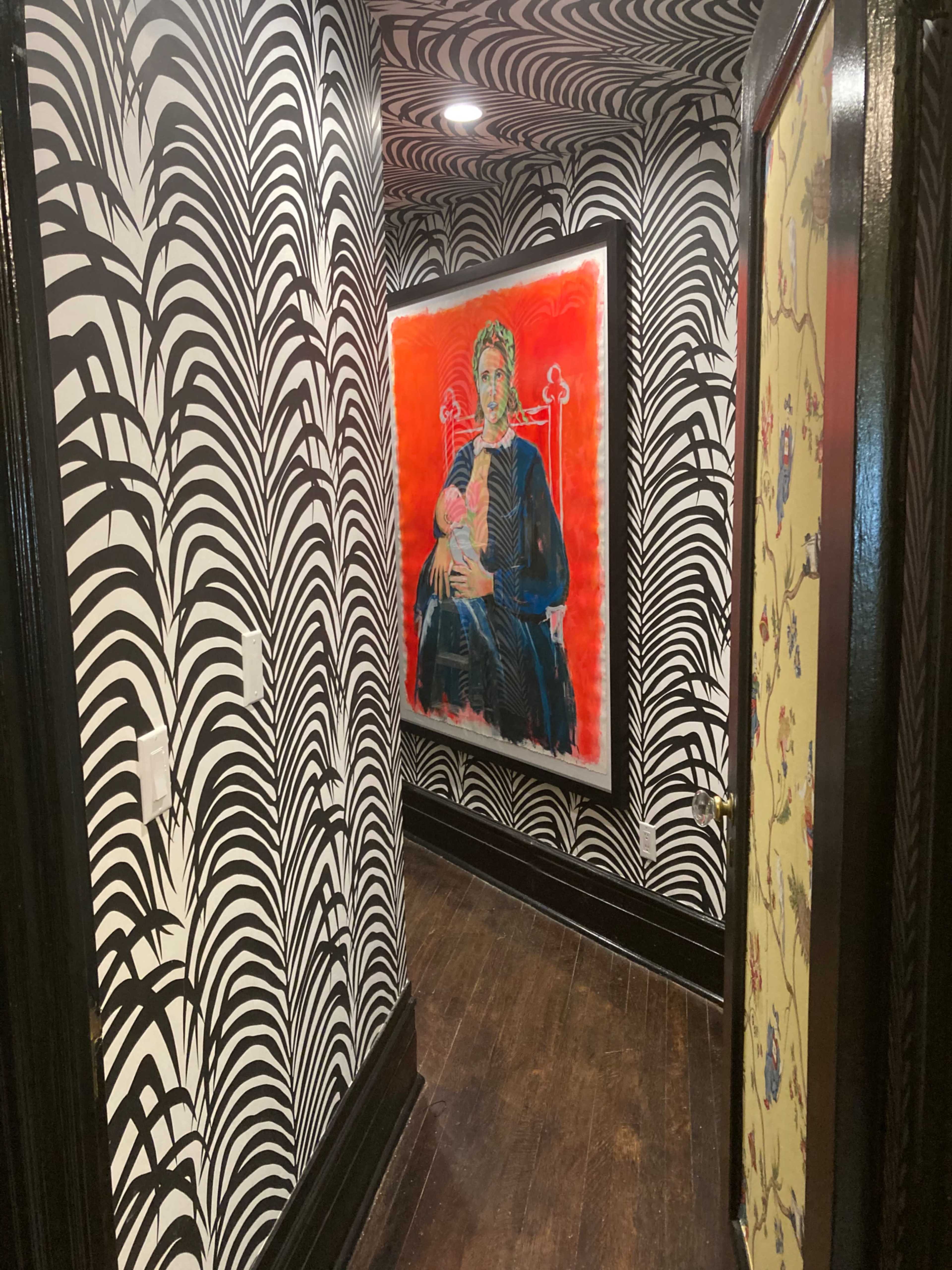 A hallway lined with black and white patterned wallpaper features an artwork of a seated figure against a bright red background.