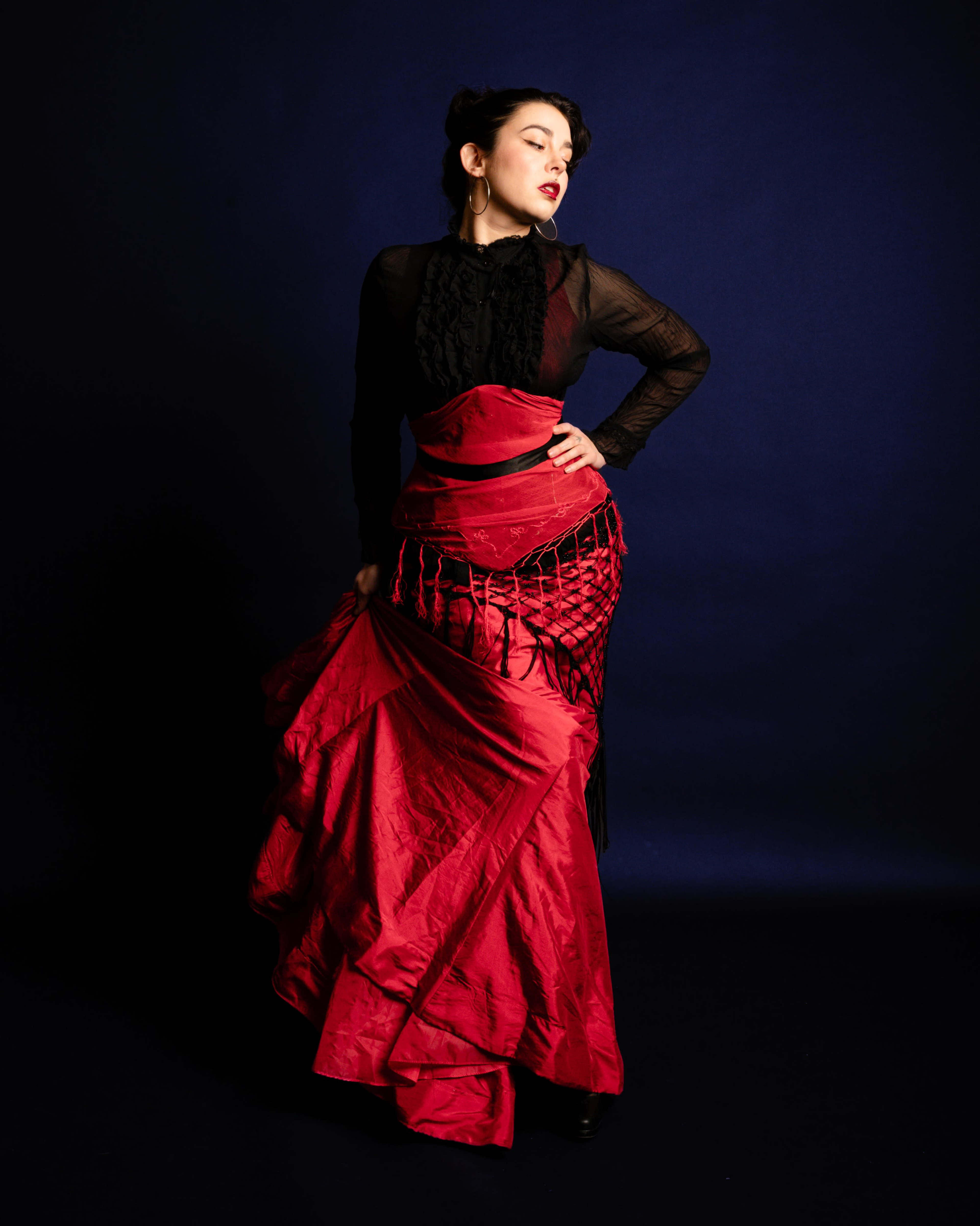 A woman poses in a dramatic red gown with a structured silhouette against a dark blue background.