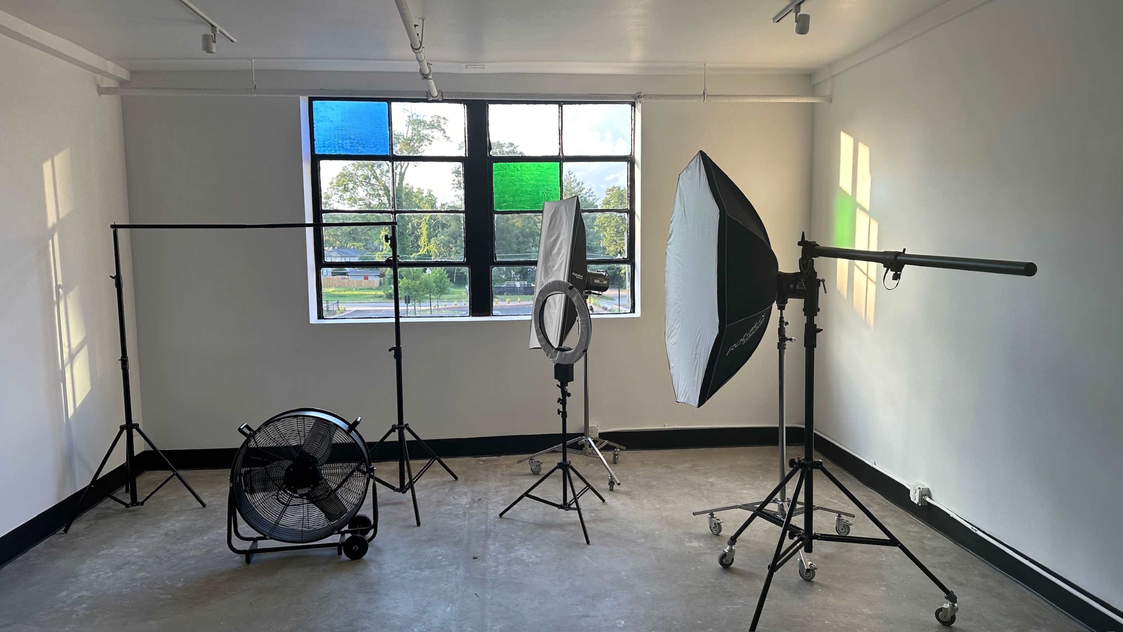 A photography studio featuring various lighting equipment, a fan, and a large window with colorful panes.