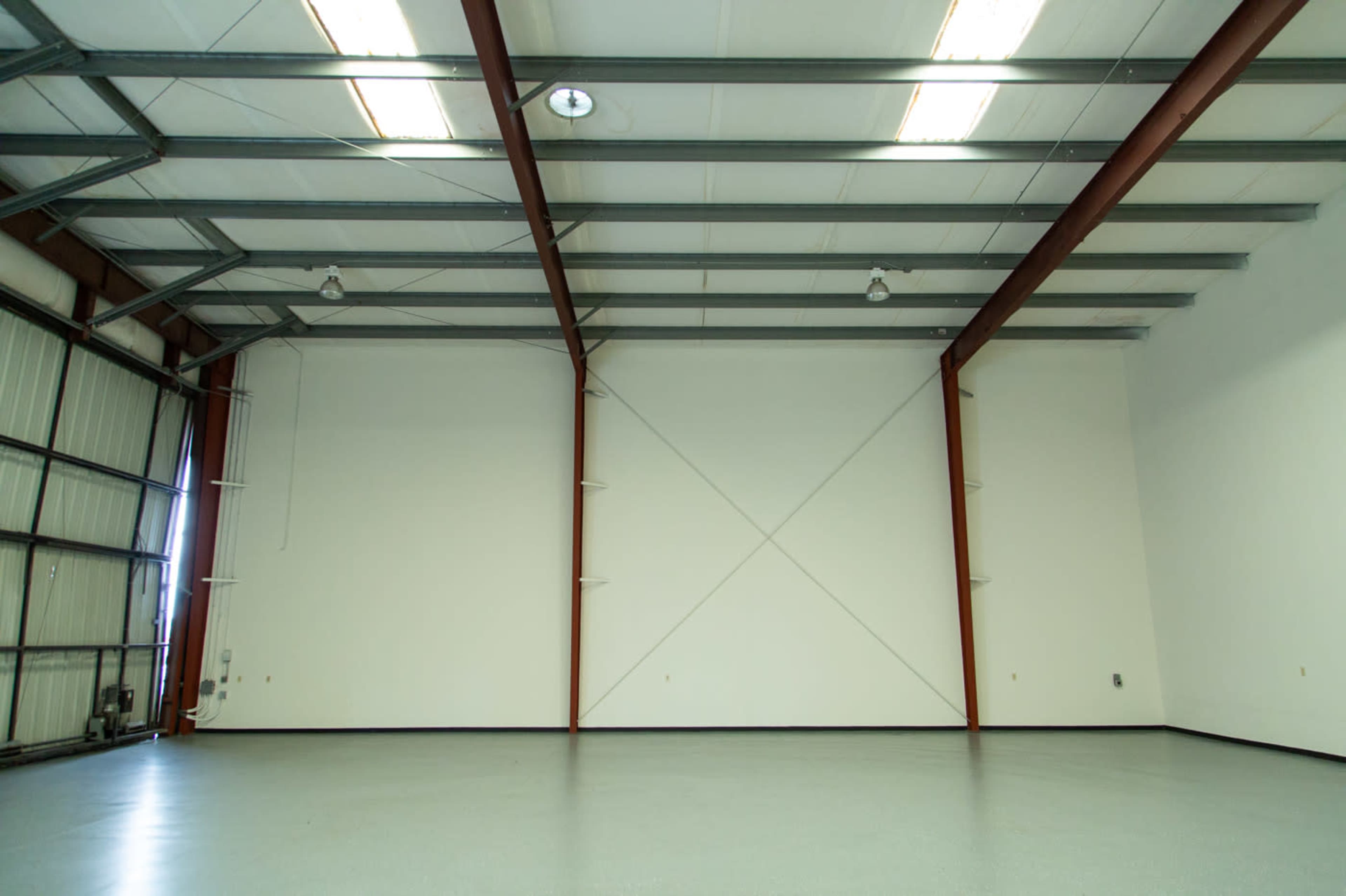A spacious industrial room with a high ceiling, metal beams, and a smooth concrete floor.