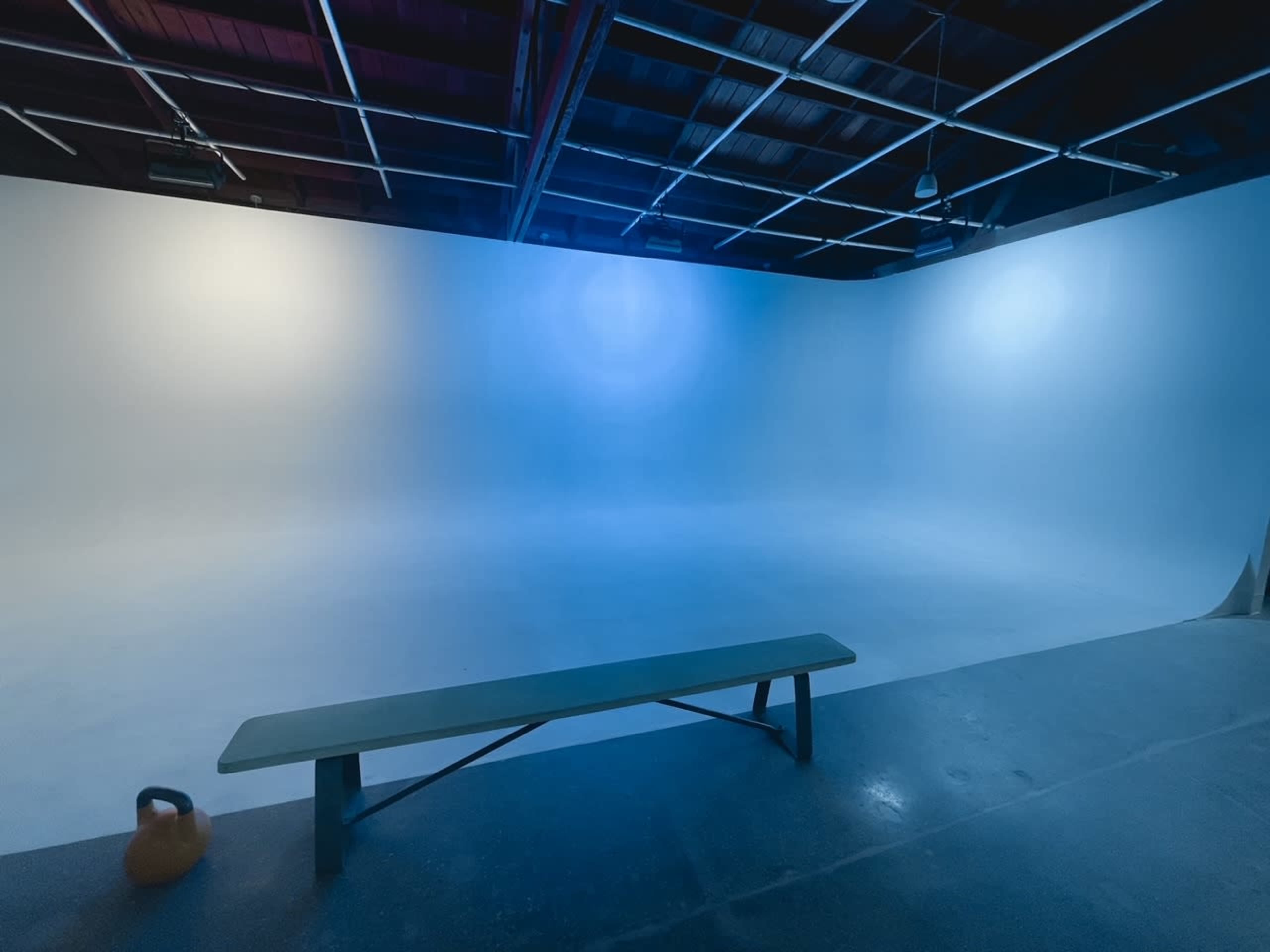 An empty photo studio with a smooth gradient backdrop and a wooden bench beside a kettlebell.