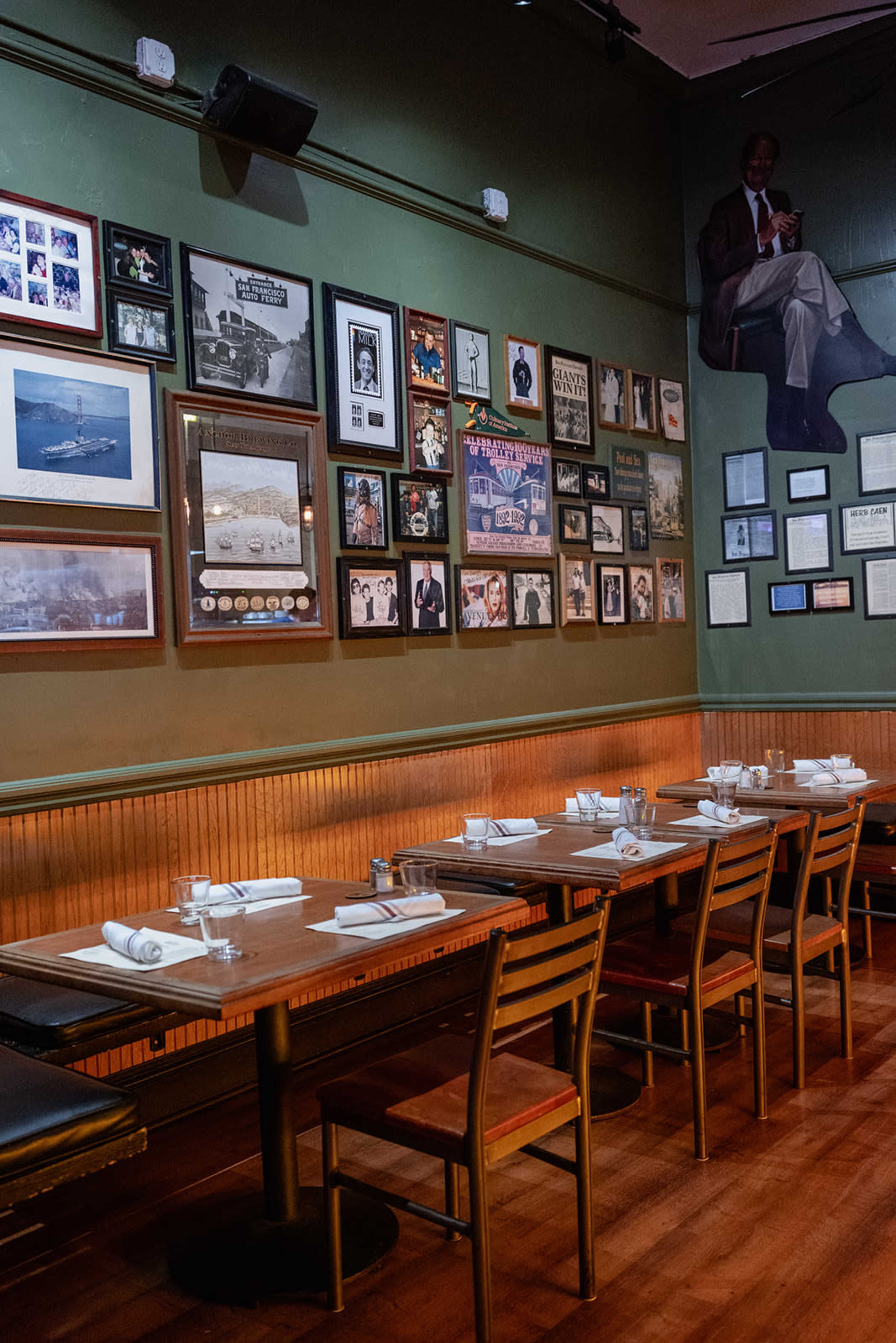 The image shows a restaurant interior featuring wooden tables with white table settings and walls adorned with various framed photographs and memorabilia.