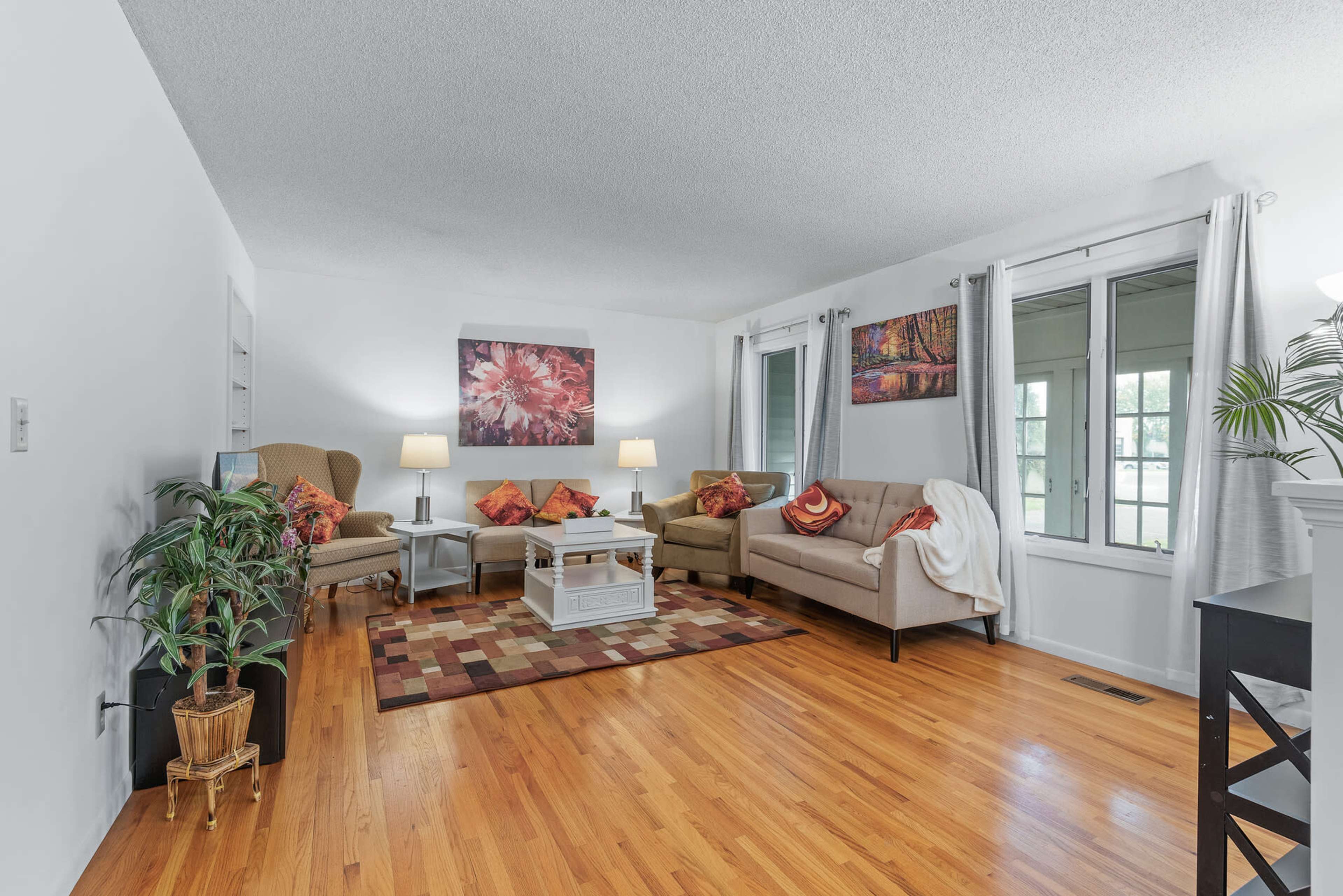 The image features a living room with two sofas and an armchair, a coffee table, and artwork on the walls, all set on a hardwood floor with a patterned rug.