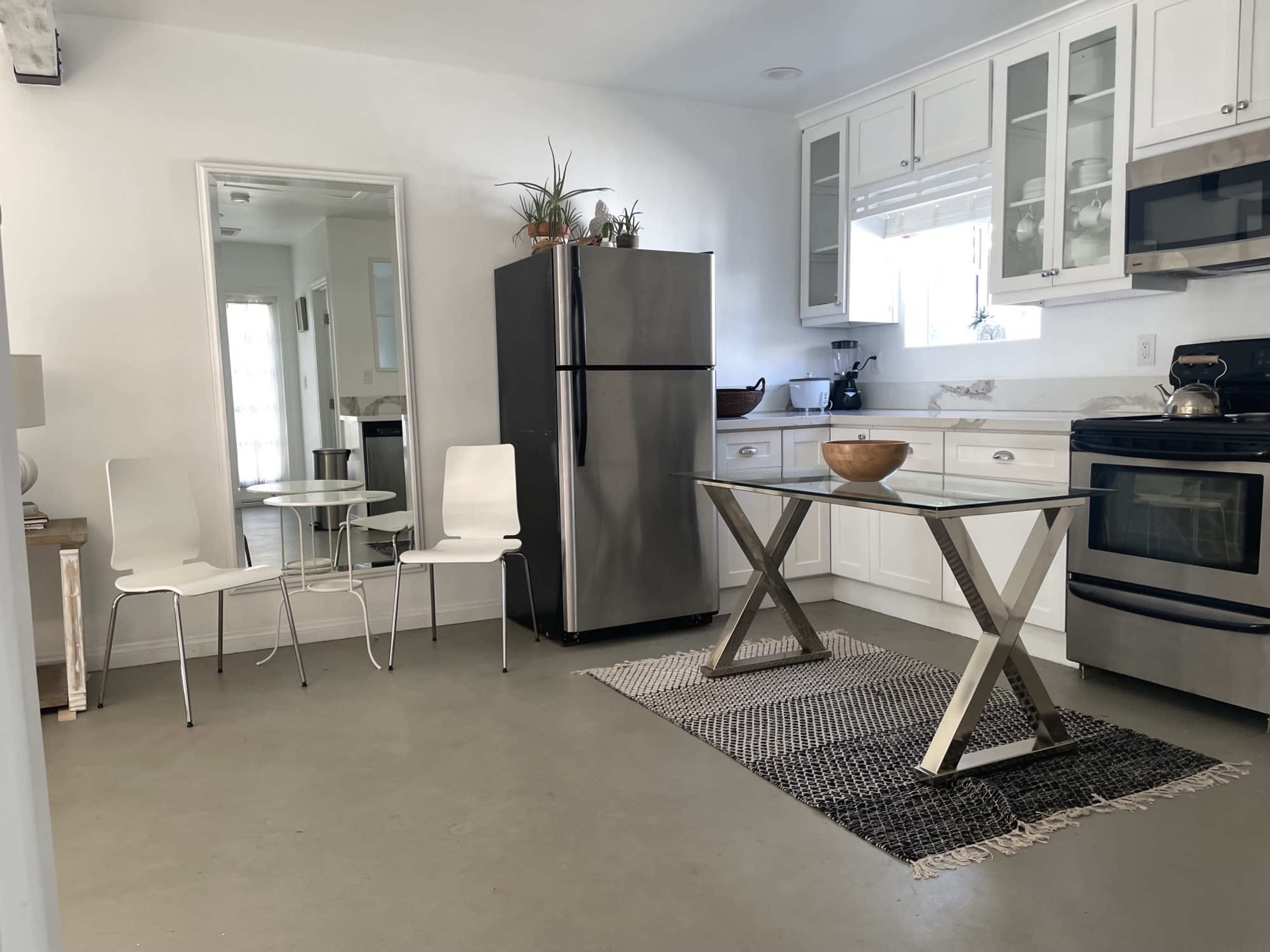 A modern kitchen with white cabinets, stainless steel appliances, a glass-top table, and two white chairs.