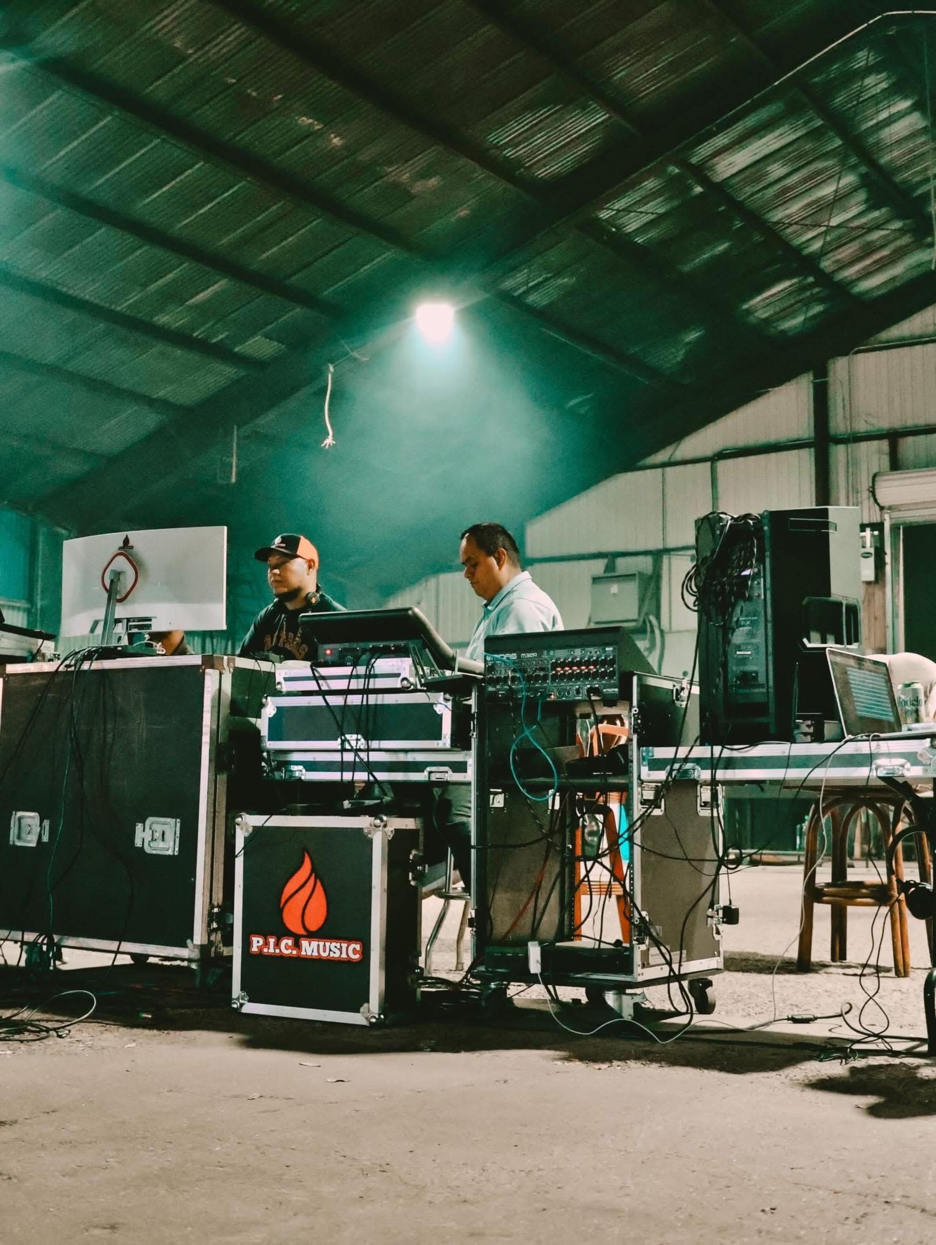 Two individuals operate audio equipment in a large, dimly lit warehouse.