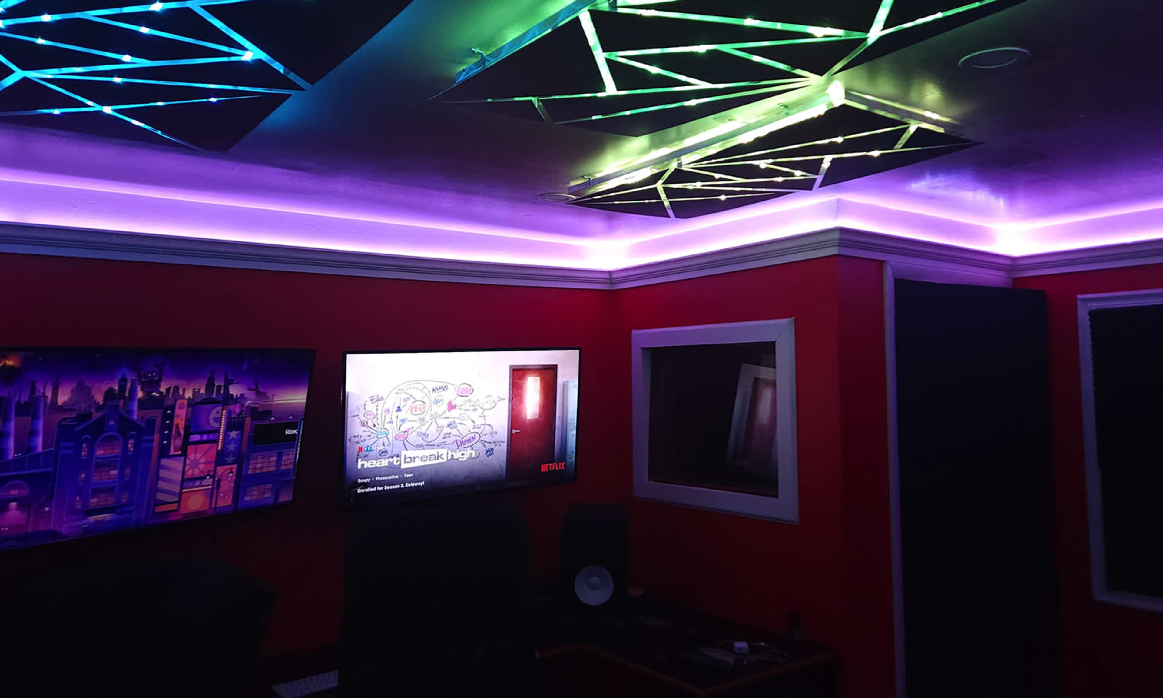 A modern room illuminated by colorful ceiling lights, featuring a television and audio equipment against red walls.