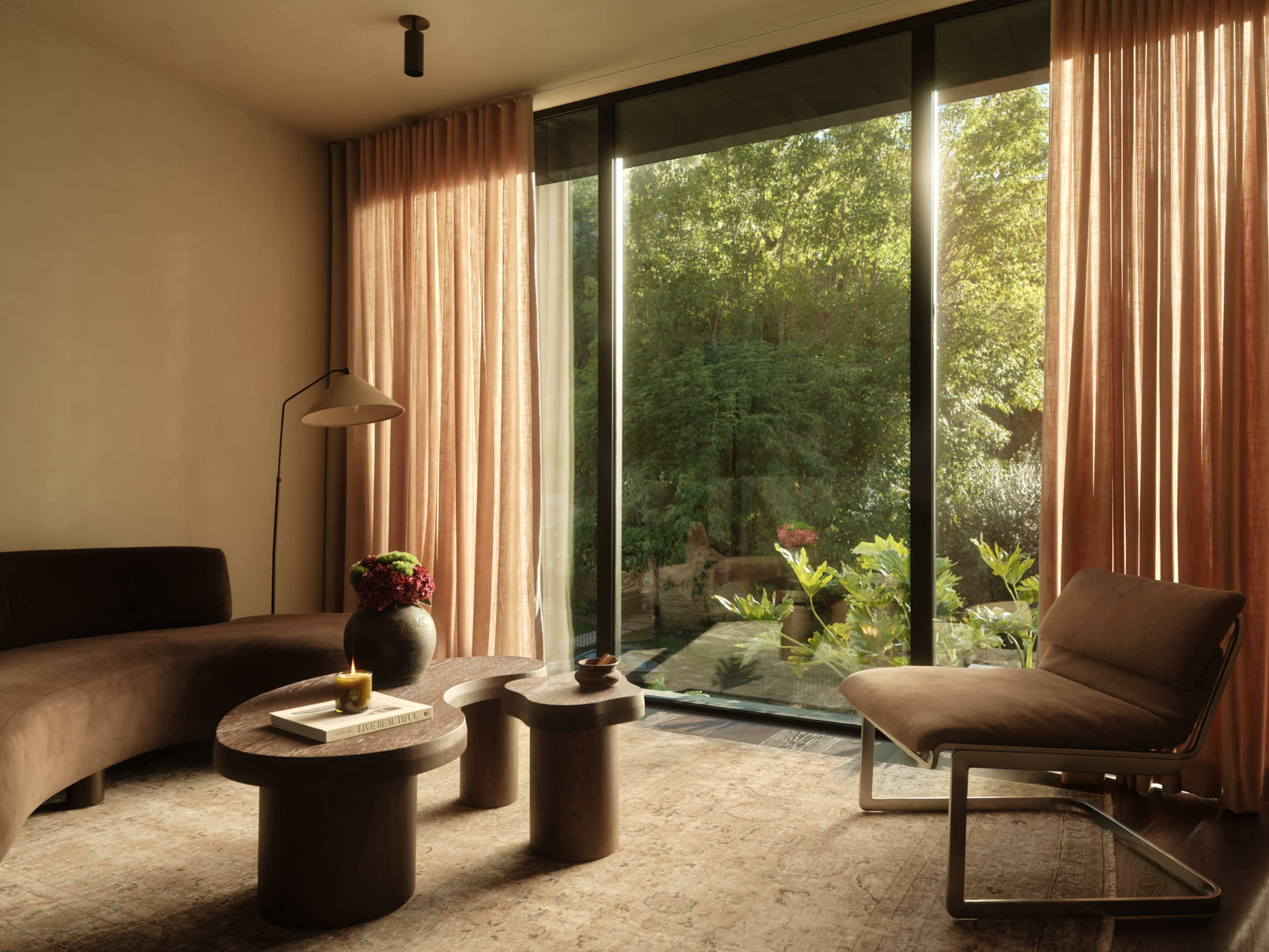 The image shows a modern living room with a curved sofa, two round side tables, and a large glass door that opens to a garden.