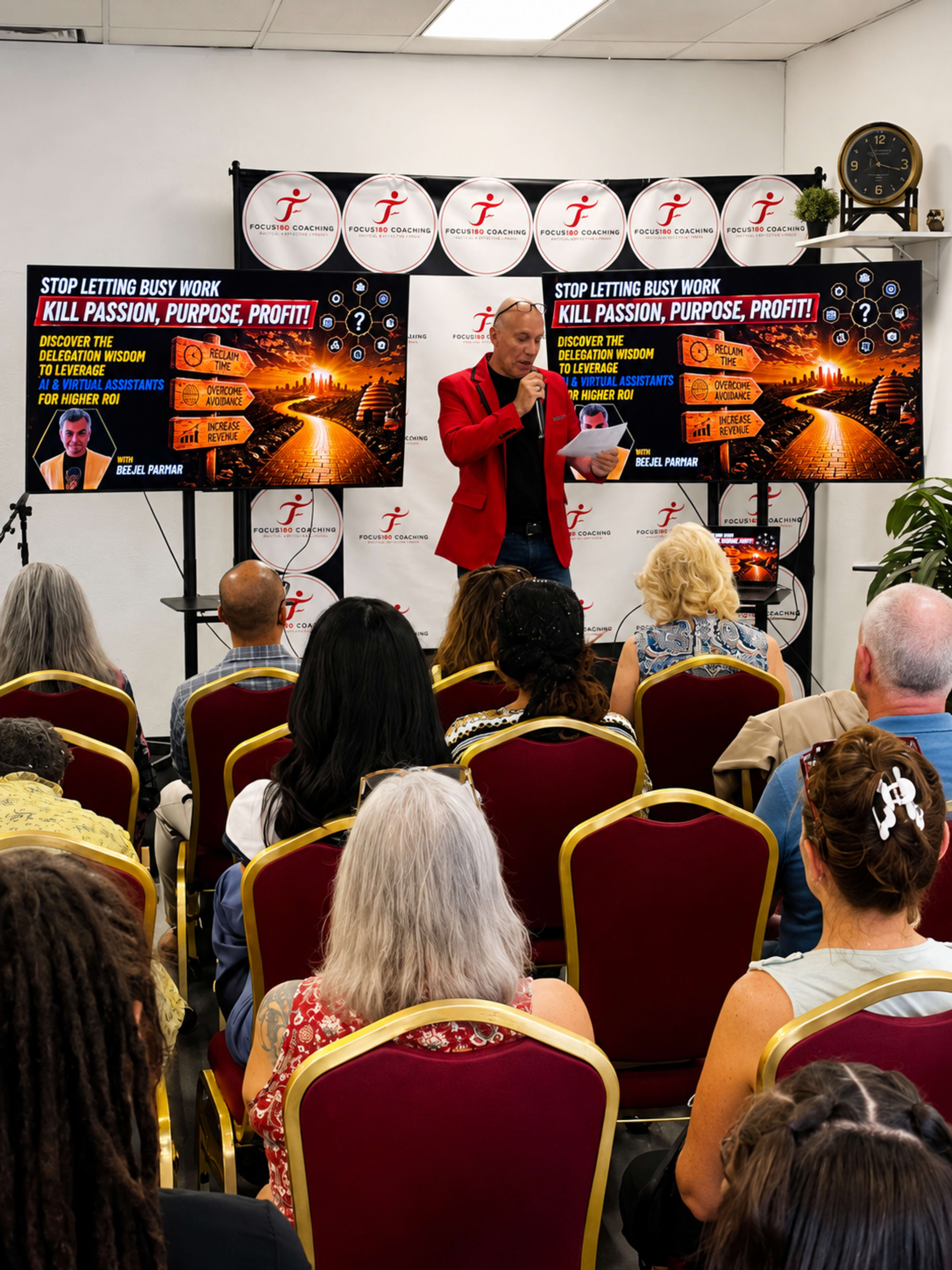 A speaker in a red blazer addresses an audience seated in a room adorned with promotional banners highlighting a motivational theme about passion and purpose.