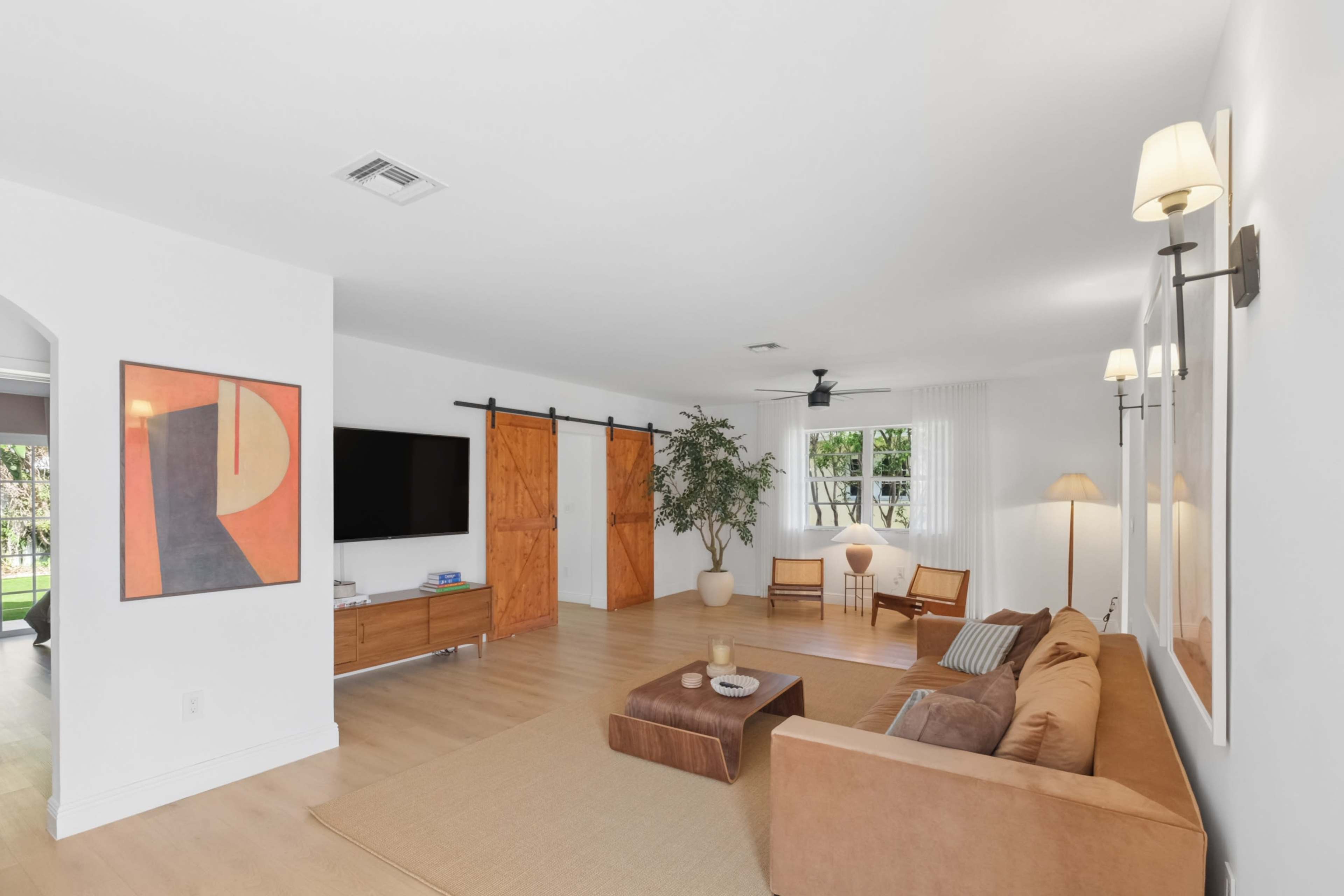The image shows a modern living room with a large sofa, a wooden coffee table, and sliding barn doors, complemented by natural light from the windows.