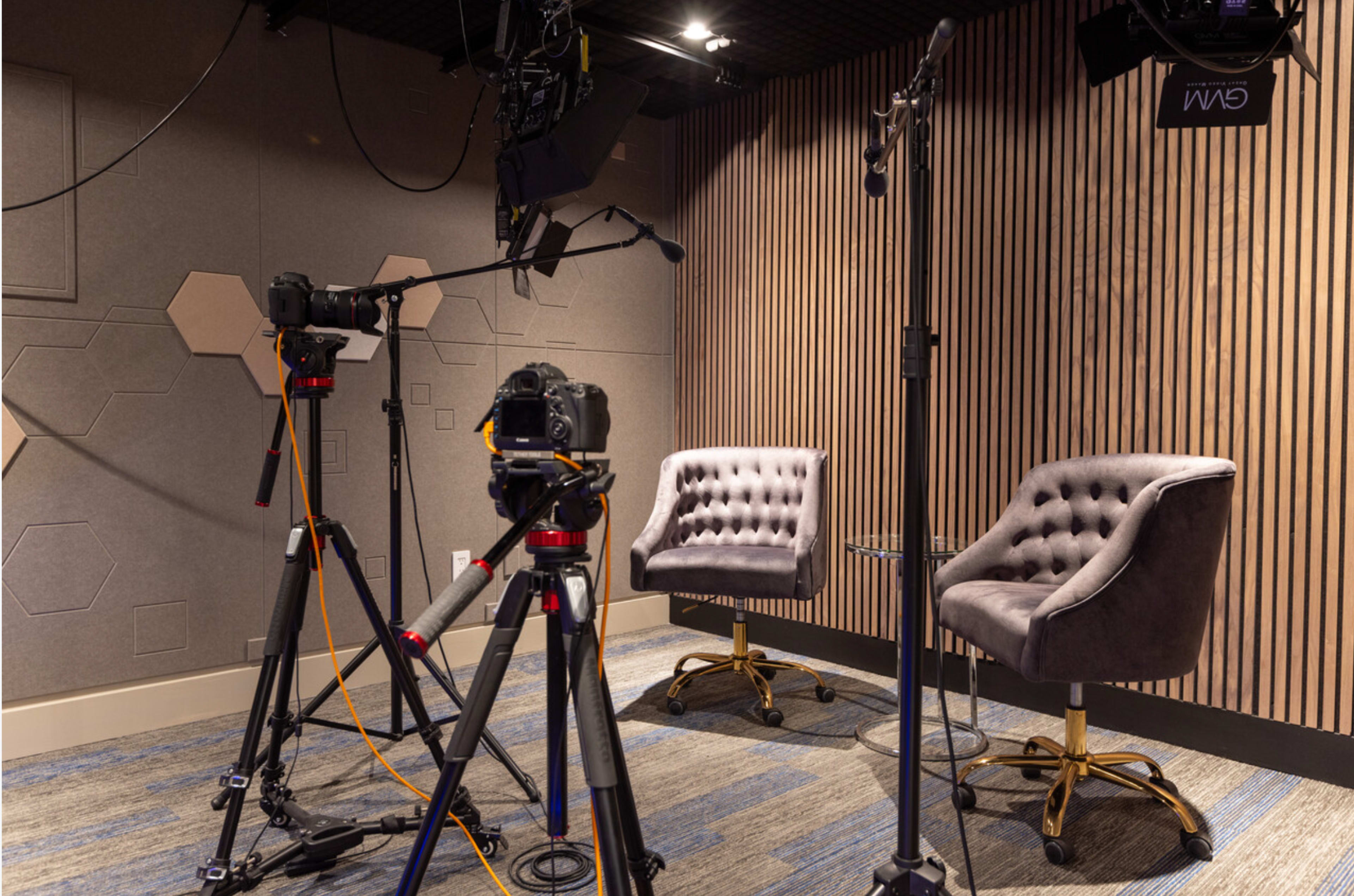 A set designed for video recording, featuring two upholstered chairs and two cameras positioned on tripods.