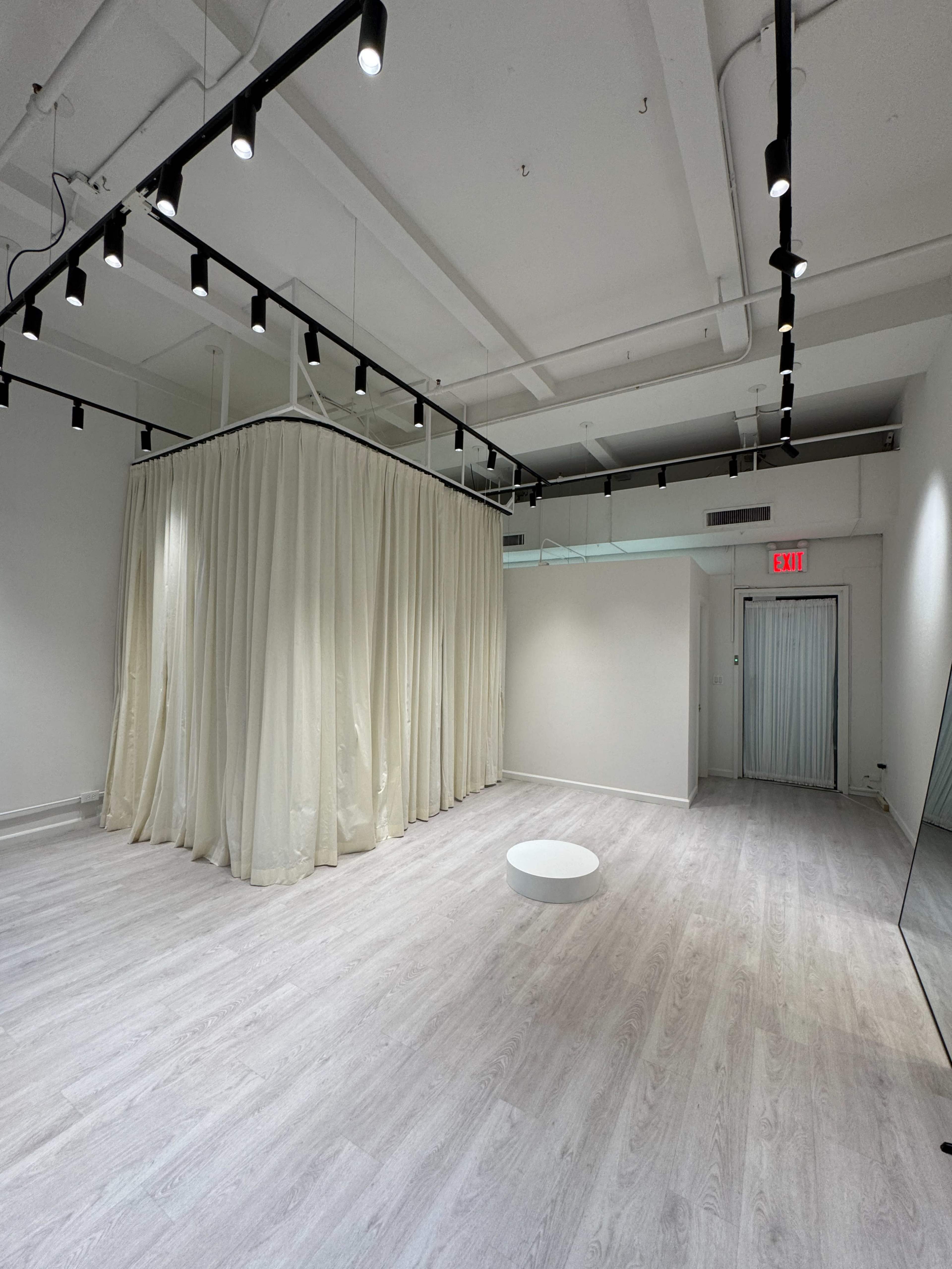 The image shows a spacious, modern room with light wood flooring, white walls, and a large curtain draped in the center, creating a distinct area within the space.