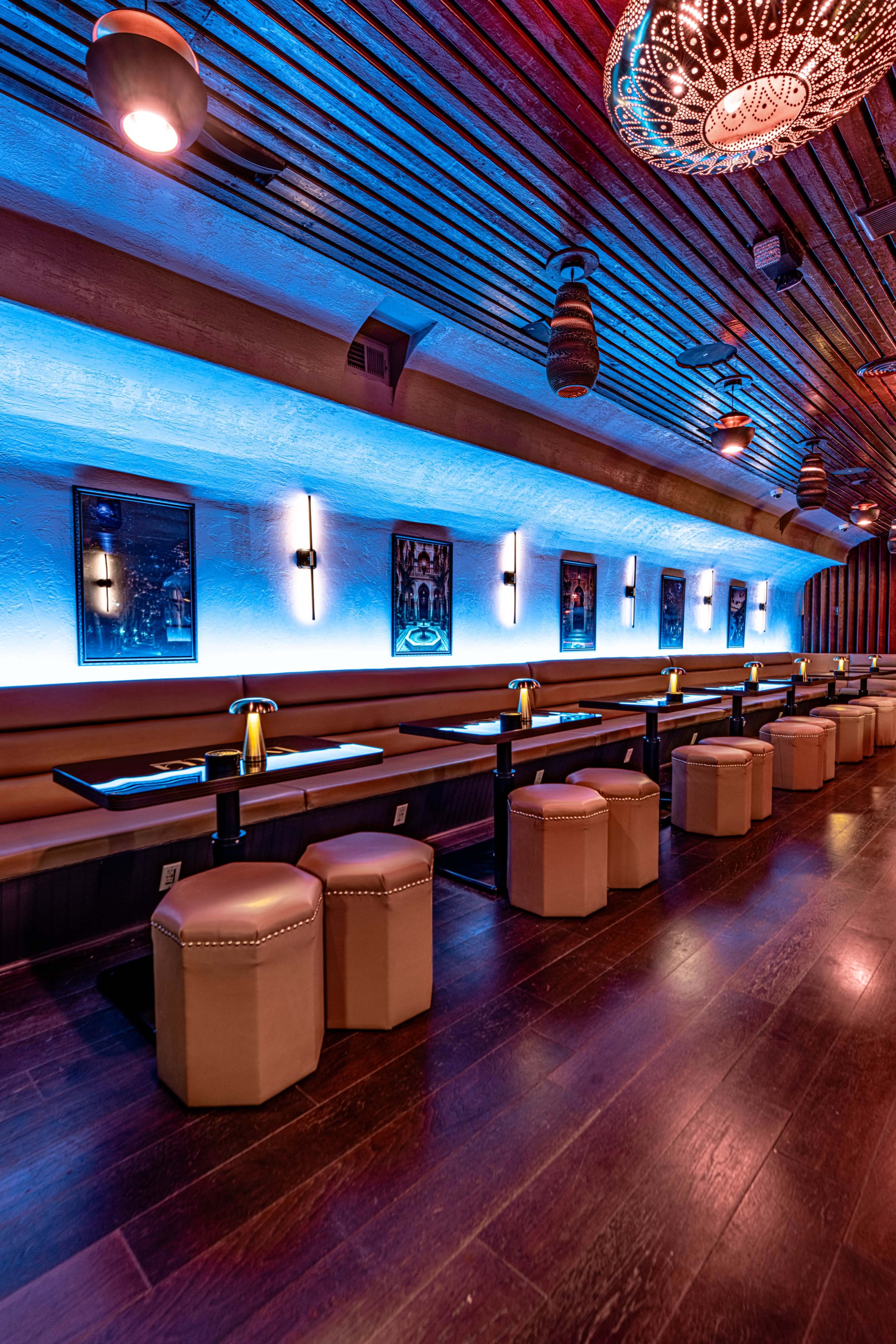 The image shows a dimly lit restaurant interior with long benches and tables, illuminated by blue lighting along the walls.