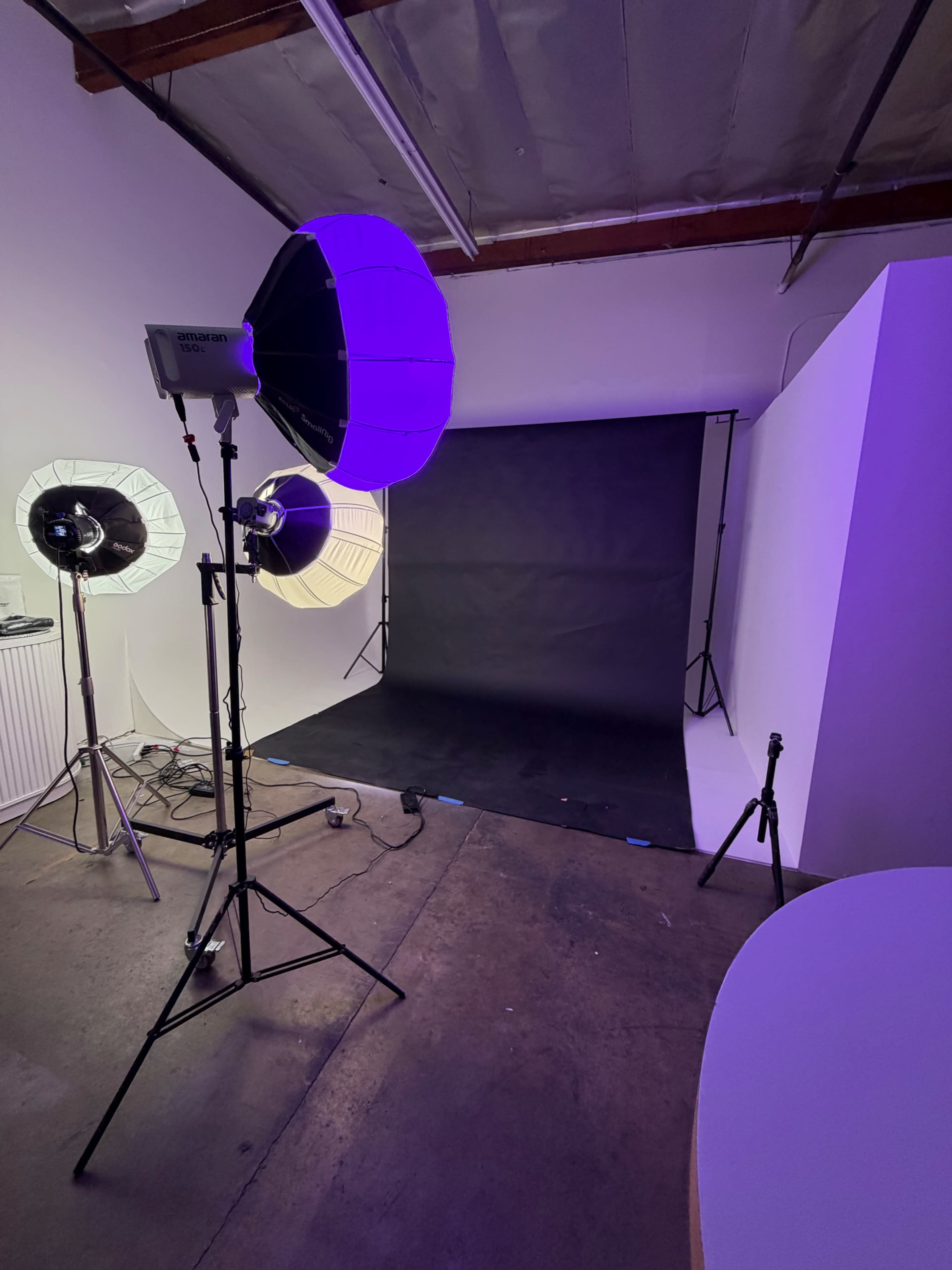 The image shows a photography studio setup with two softbox lights and a large round light aimed at a backdrop, which is set up in a corner of the room.
