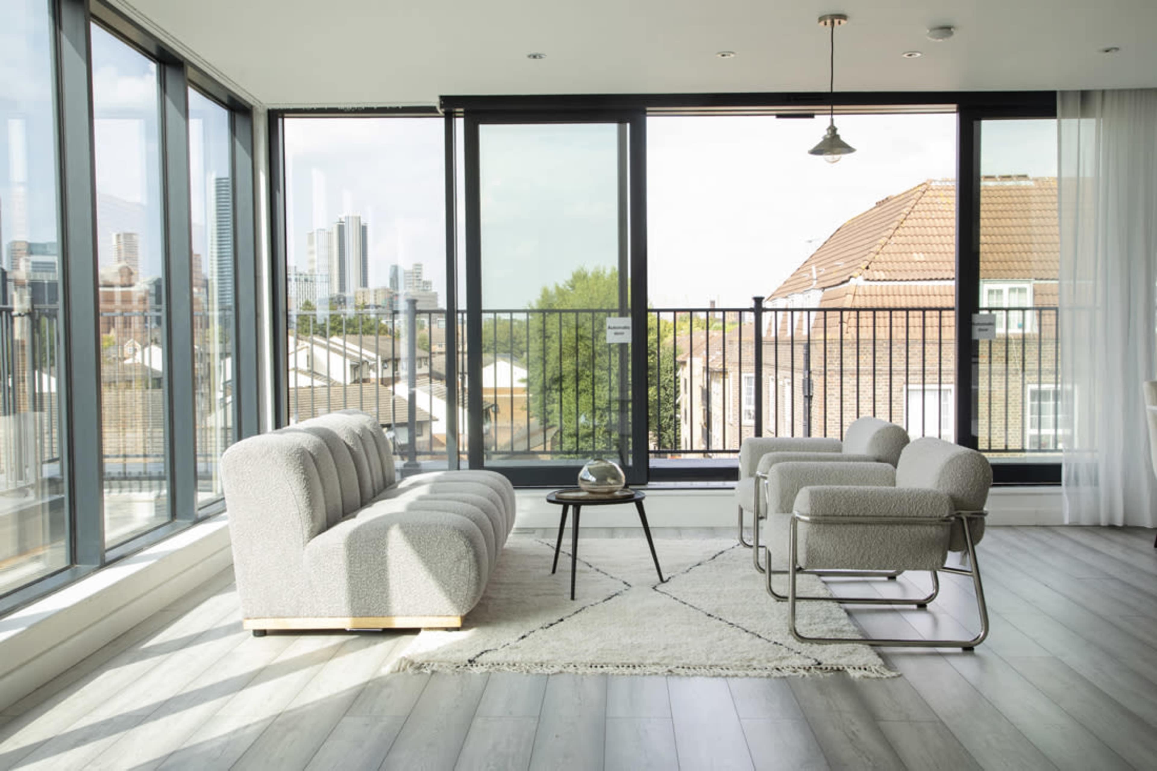 A modern living room features a gray sofa set and armchair around a small table, with large windows overlooking a cityscape.