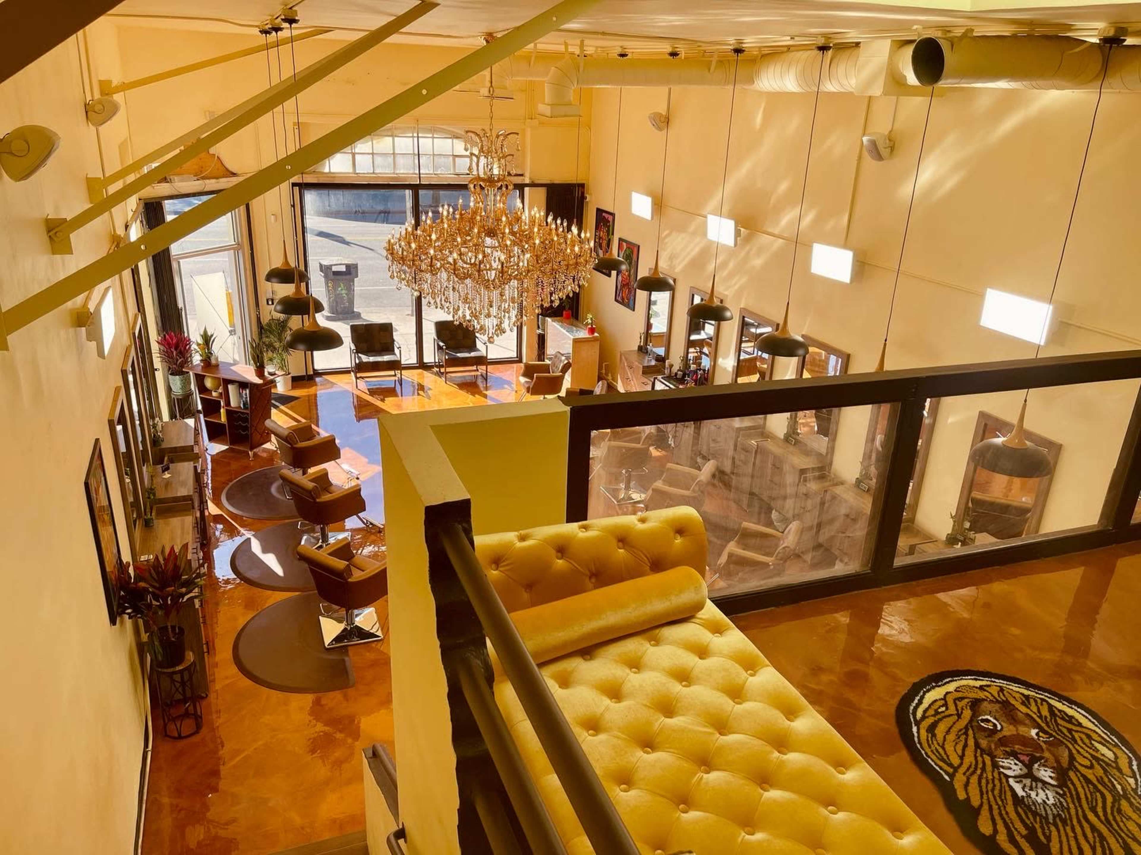 A spacious, well-lit interior with a chandelier, seating areas, and large windows, viewed from an upper level.