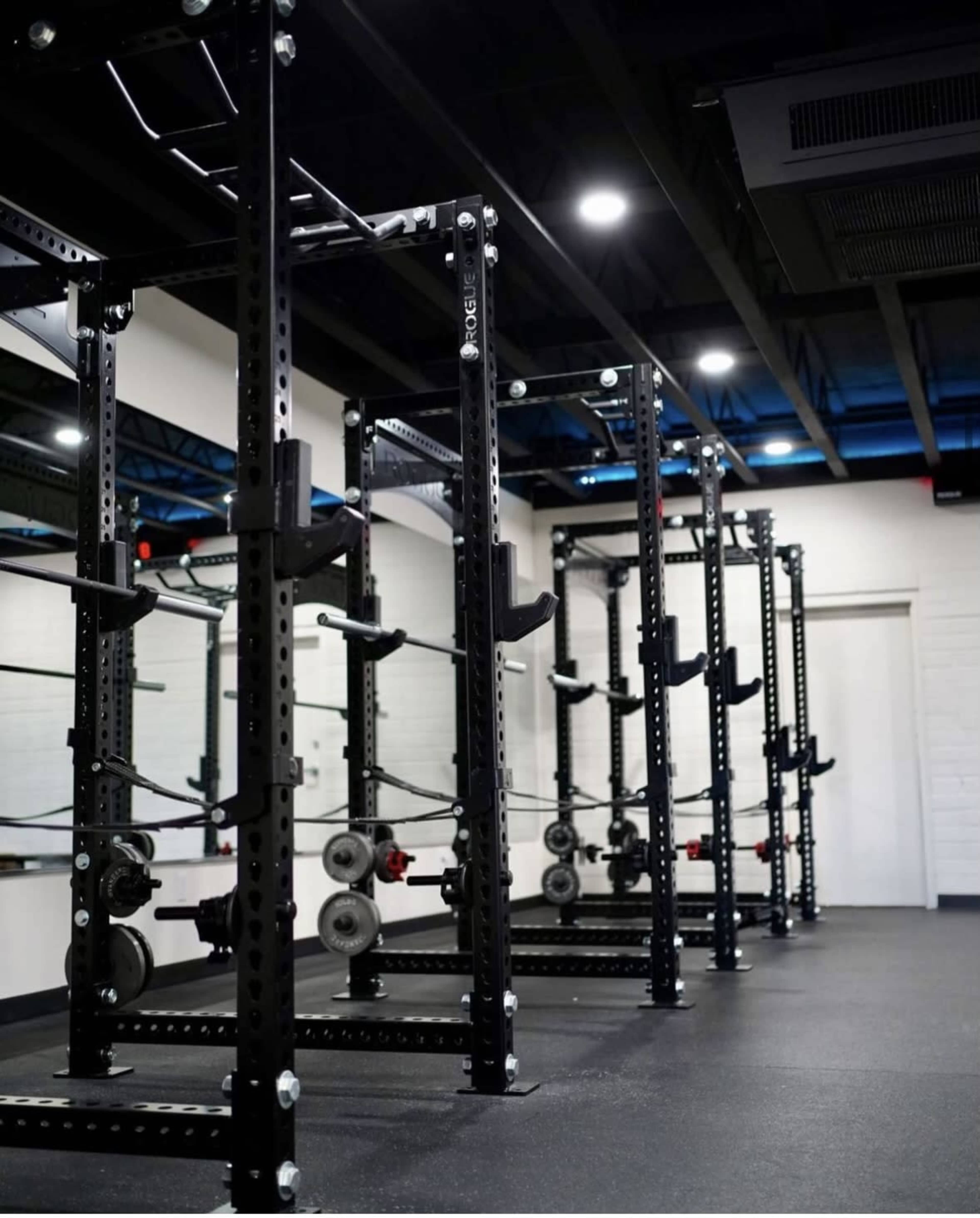 The image shows a row of black weightlifting racks arranged in a gym with a minimalist design.