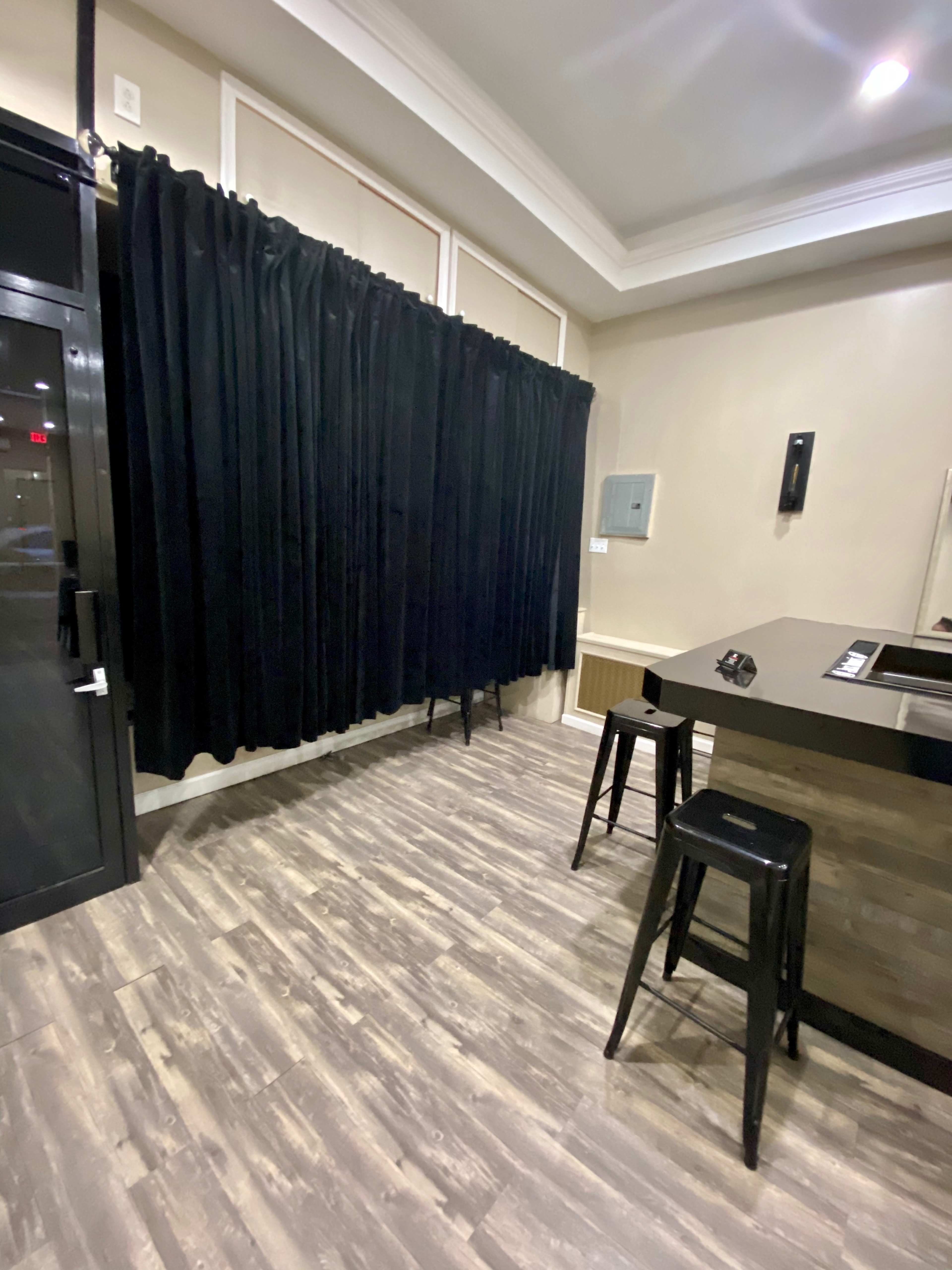 The image shows a room with black curtains covering a wall, a bar with stools, and wooden flooring.