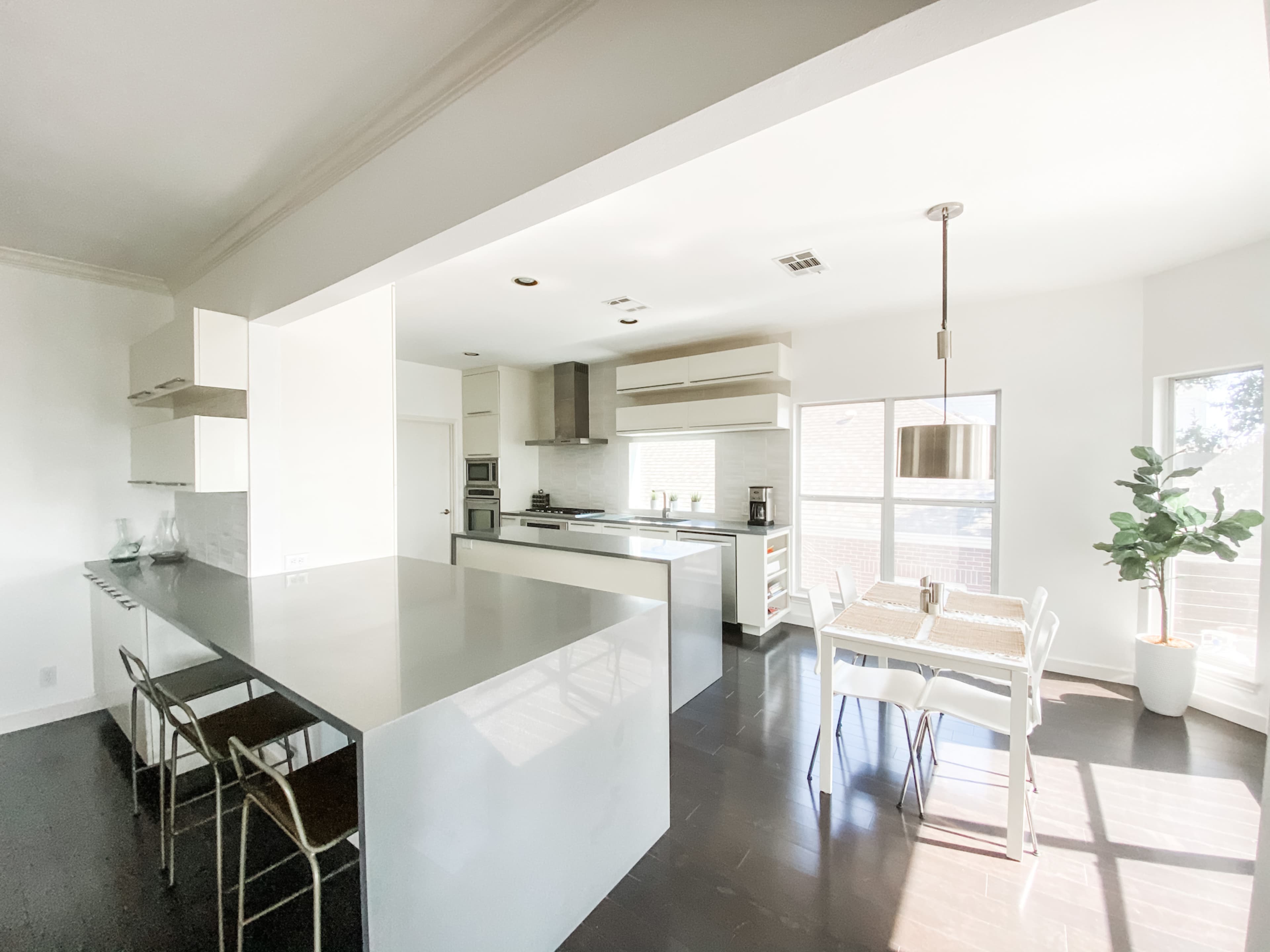 A modern kitchen features a large island, sleek cabinetry, and a dining area with a table and chairs beside a window.