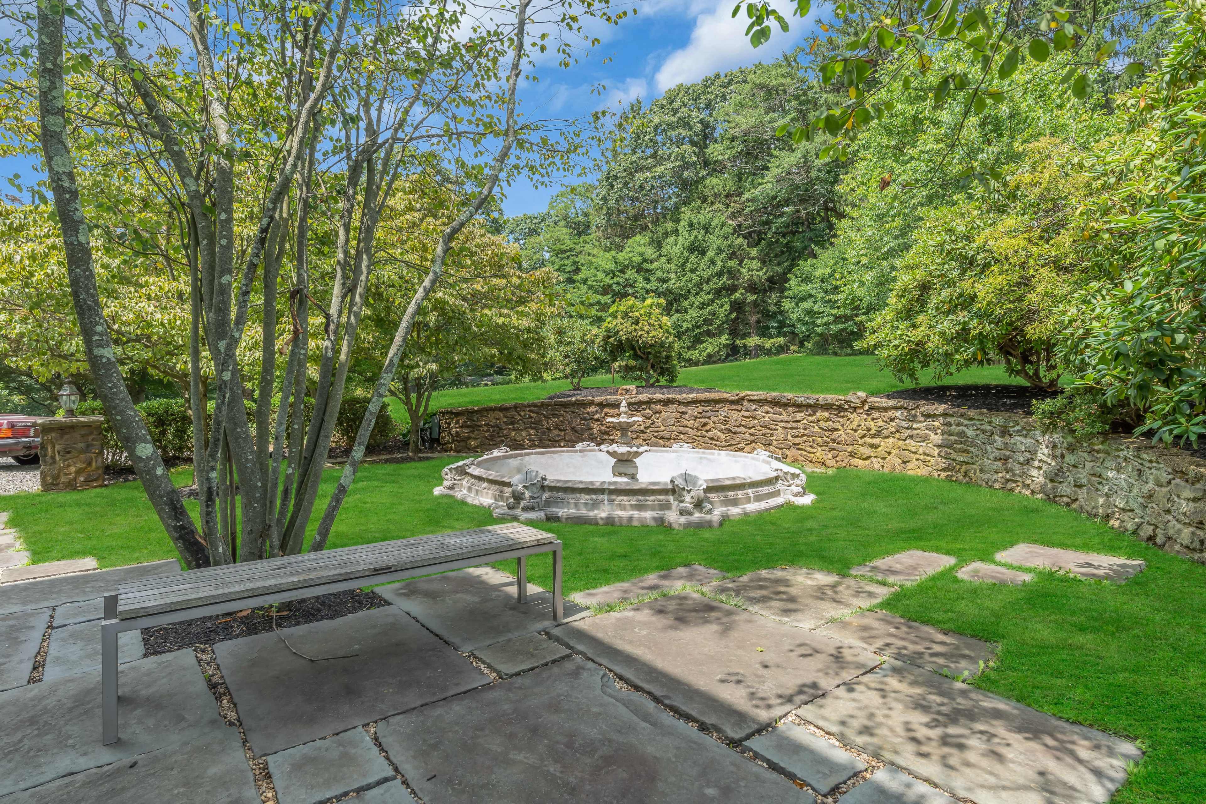 A stone fountain is surrounded by grass and trees in a landscaped garden.