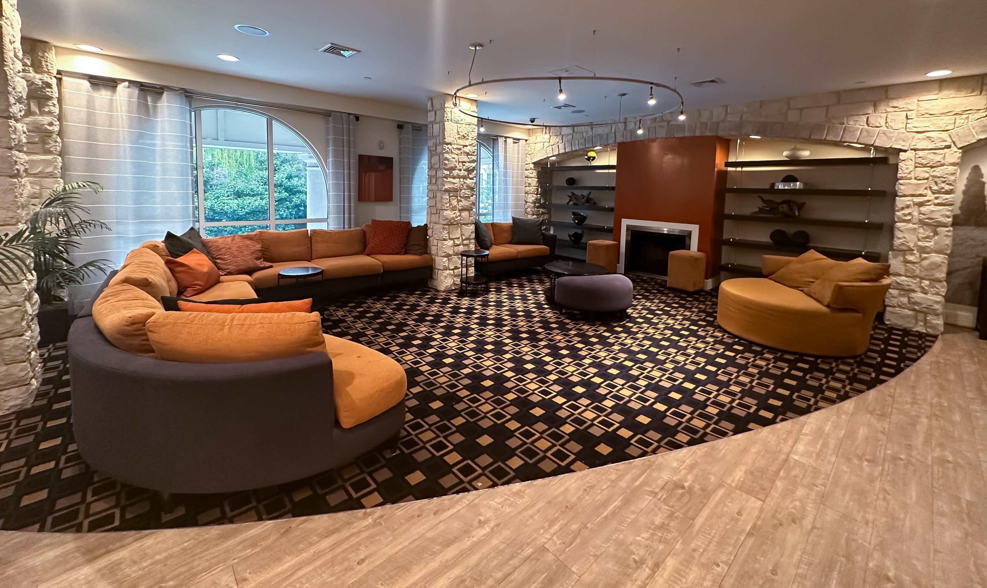 A modern lounge area with a circular arrangement of seating, including a large sectional sofa and round chairs, surrounded by stone walls and a decorative rug.