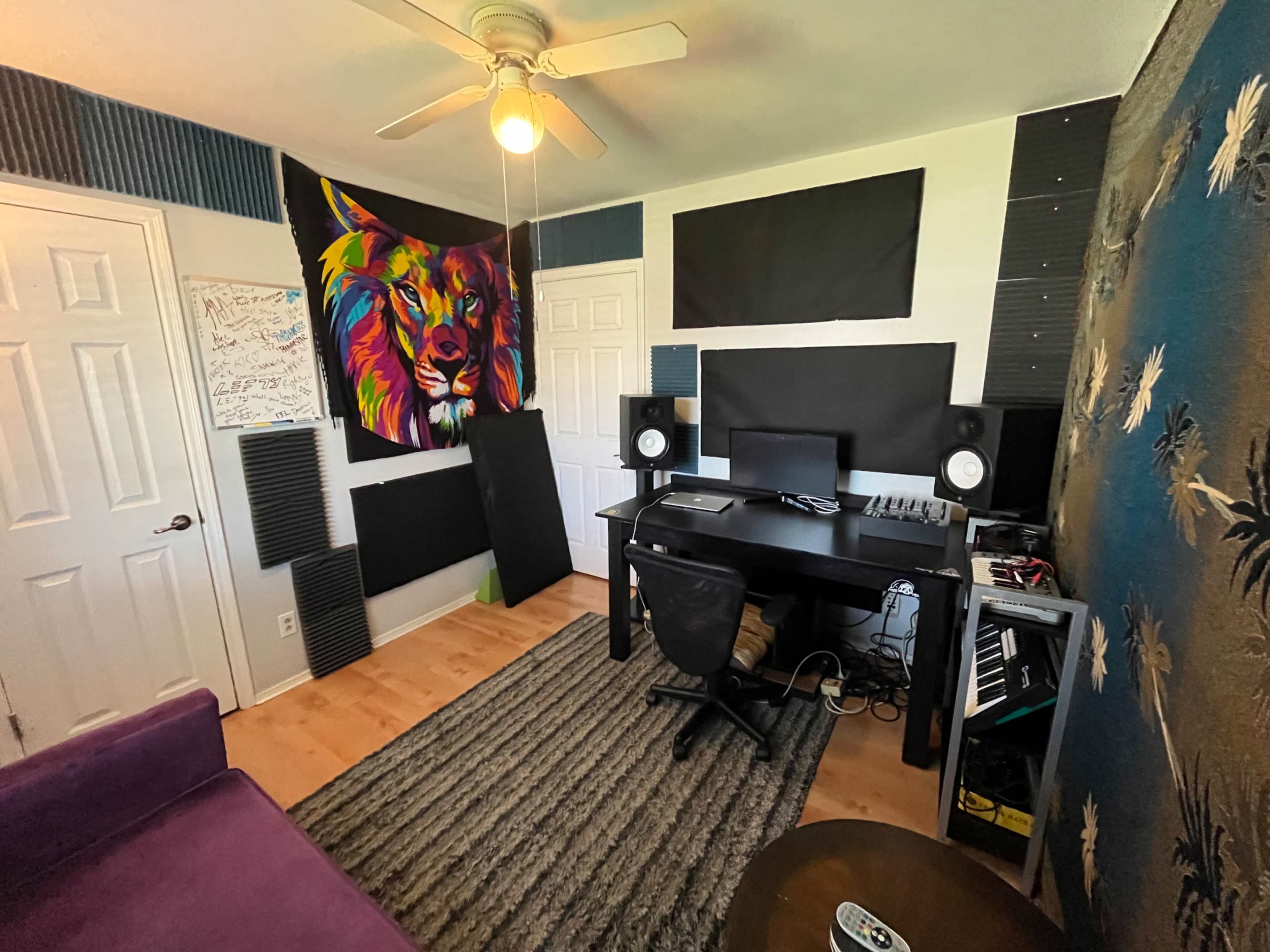 The image shows a music production studio with a desk, computer monitors, speakers, and colorful wall art, along with seating and soundproofing panels.