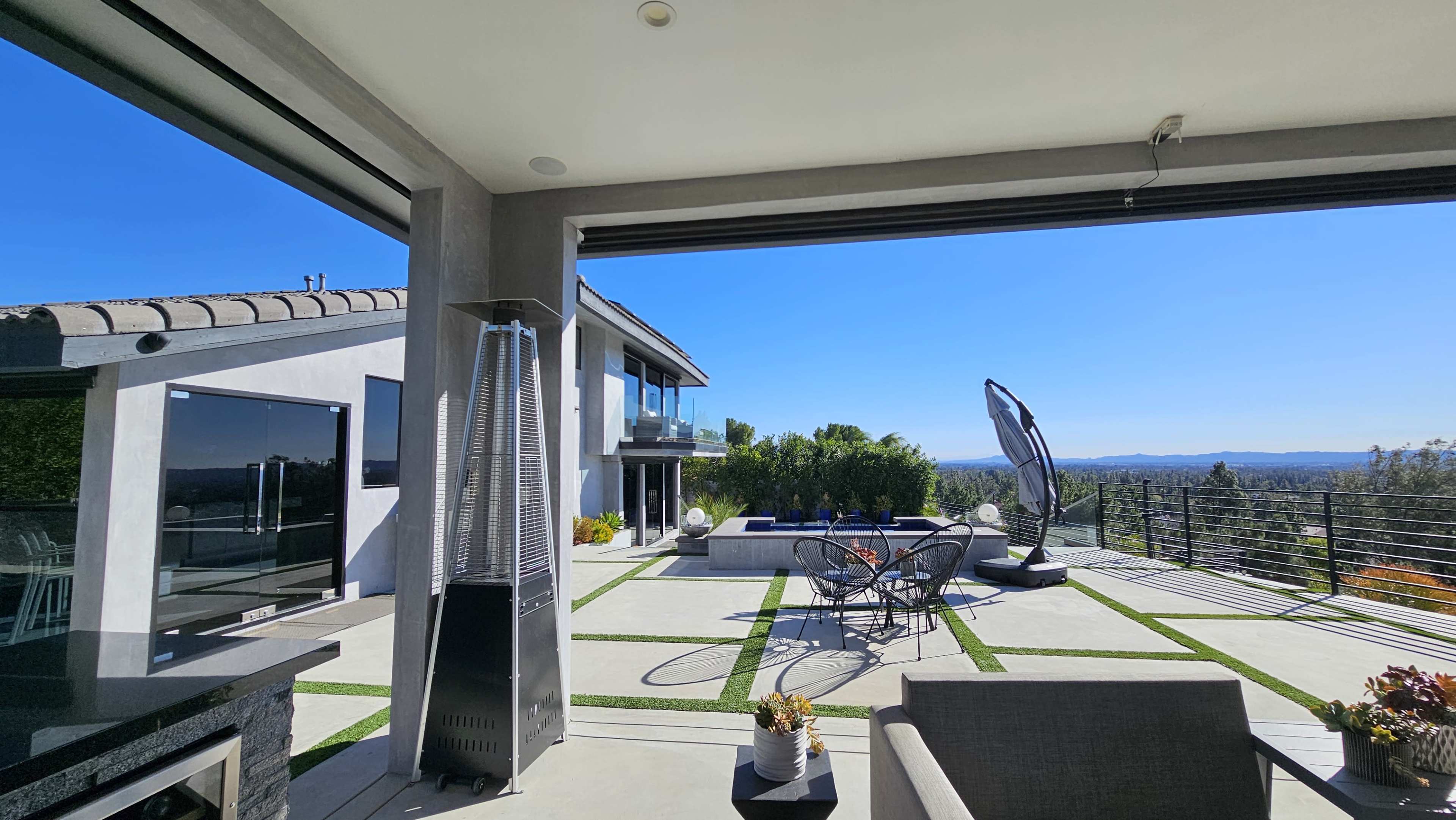 The image showcases a modern patio with outdoor seating, a fire pit, and a scenic view of distant hills and clear blue skies.