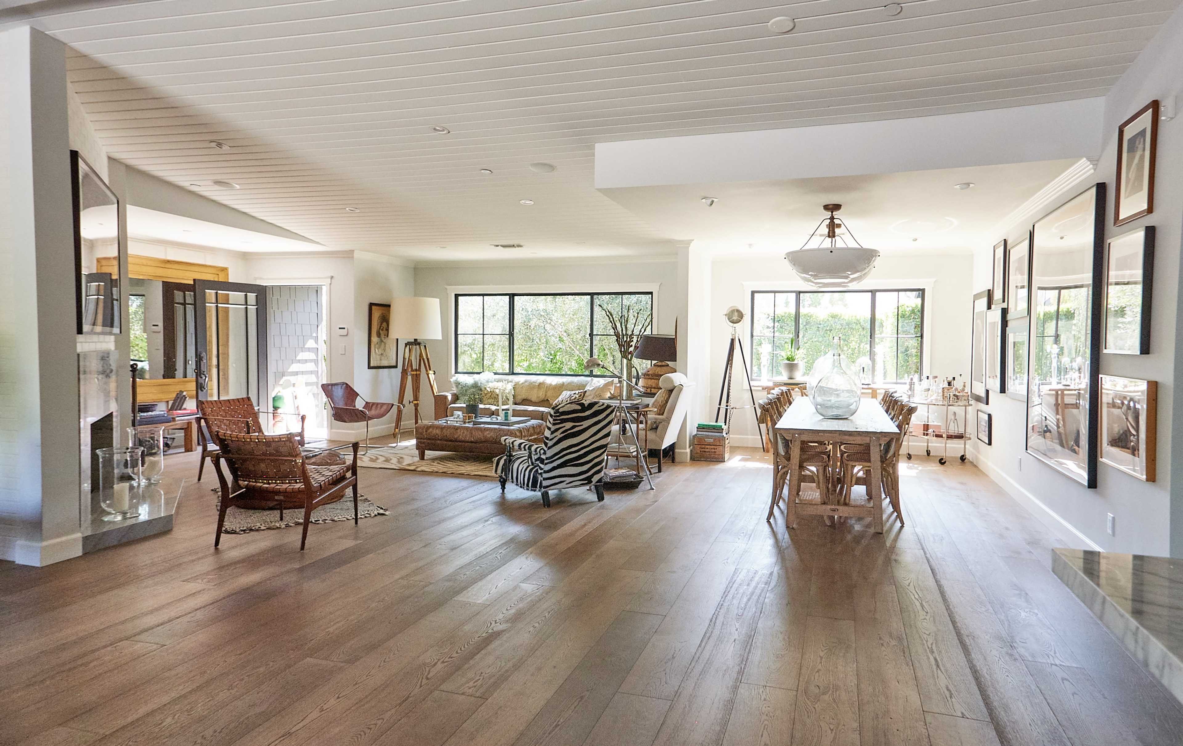 The image shows a spacious living area featuring a mix of seating arrangements, large windows, and wooden flooring.
