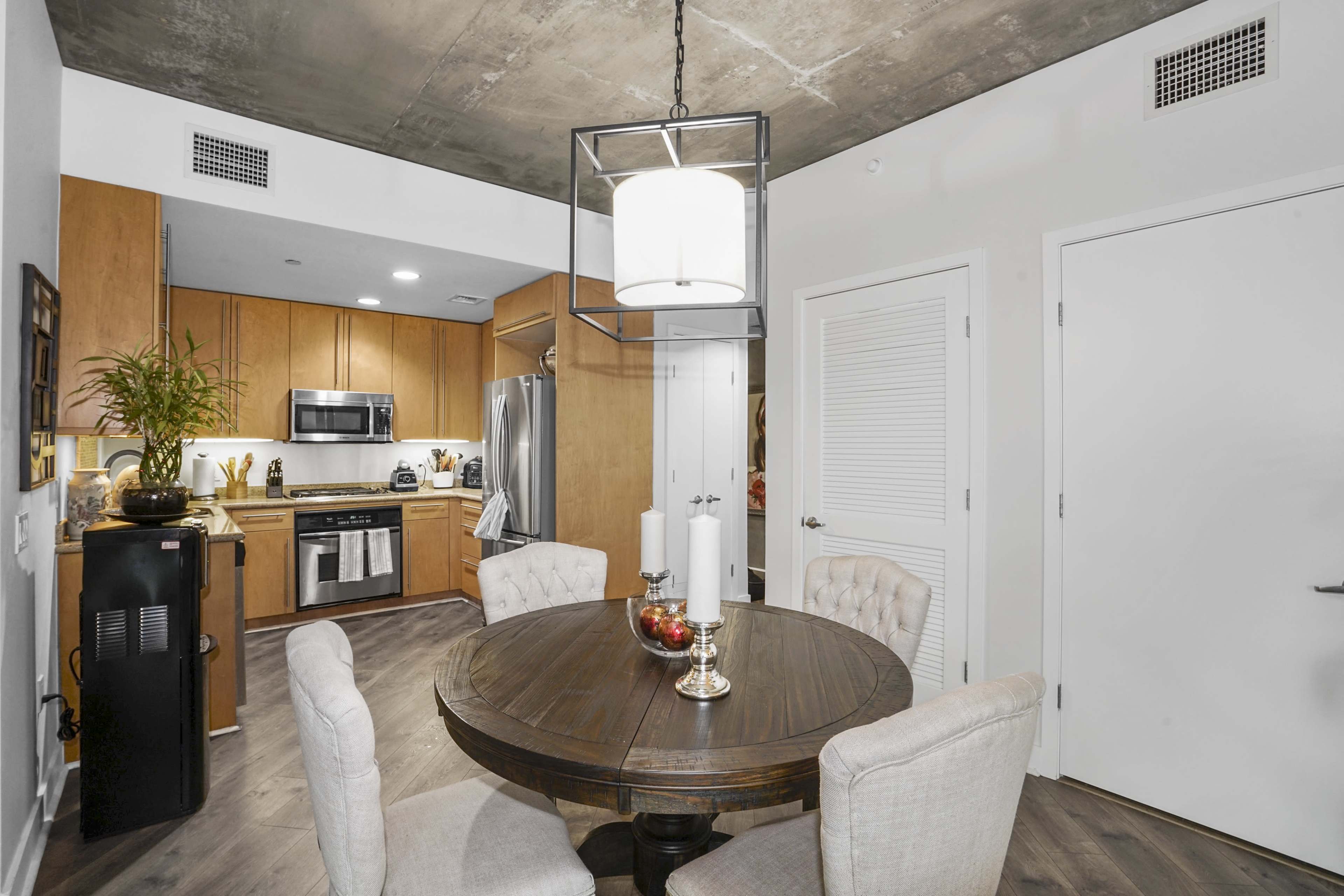 A modern kitchen and dining area with a round wooden table, four upholstered chairs, and stainless steel appliances against wooden cabinetry.