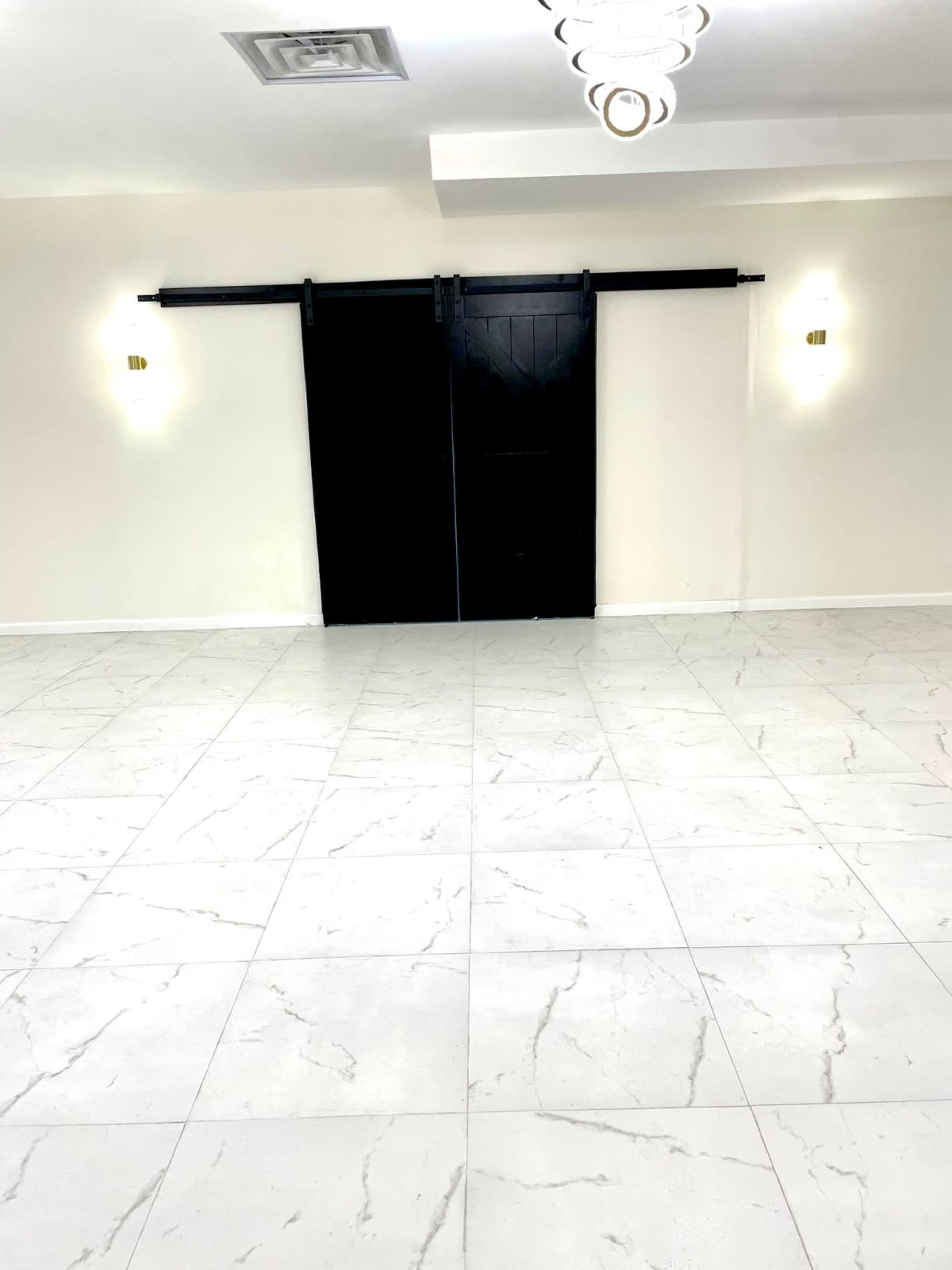 A spacious room features a large white tiled floor and a black sliding door at the far end.