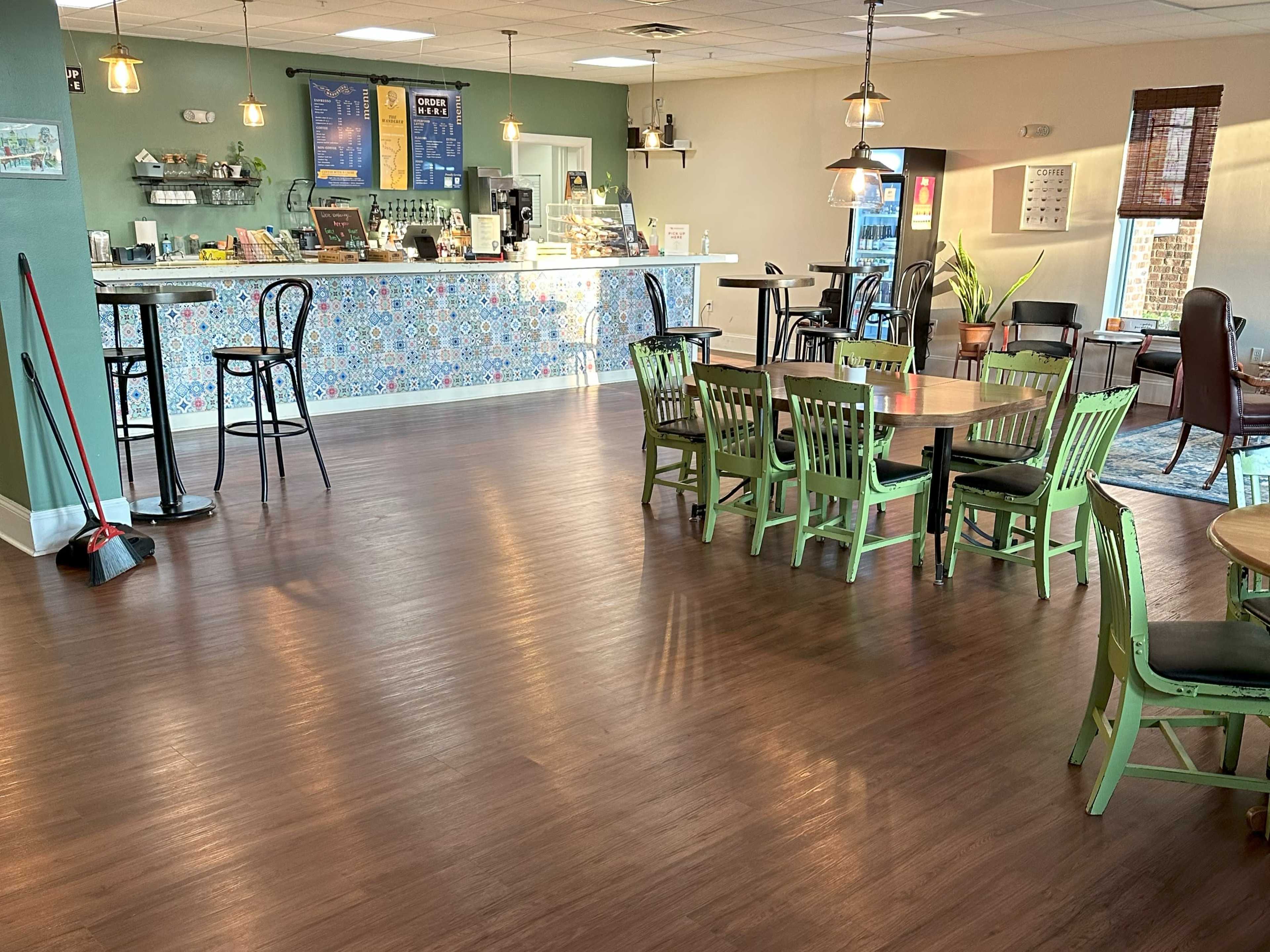 A cozy café interior with a counter displaying a menu and seating areas featuring green chairs and wooden tables.