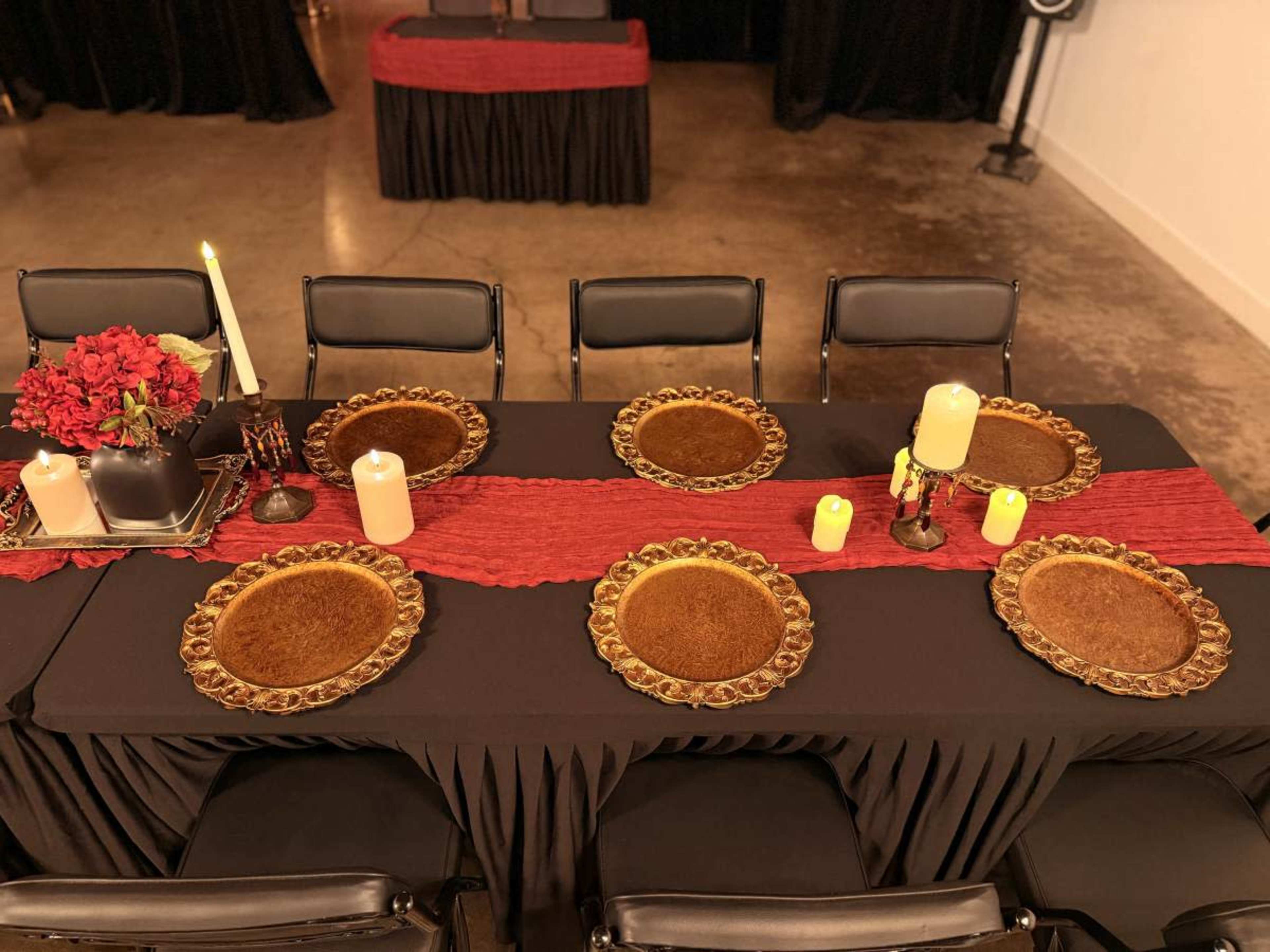 A long table is set with decorative plates, candles, and a floral arrangement, ready for a gathering or dinner event.