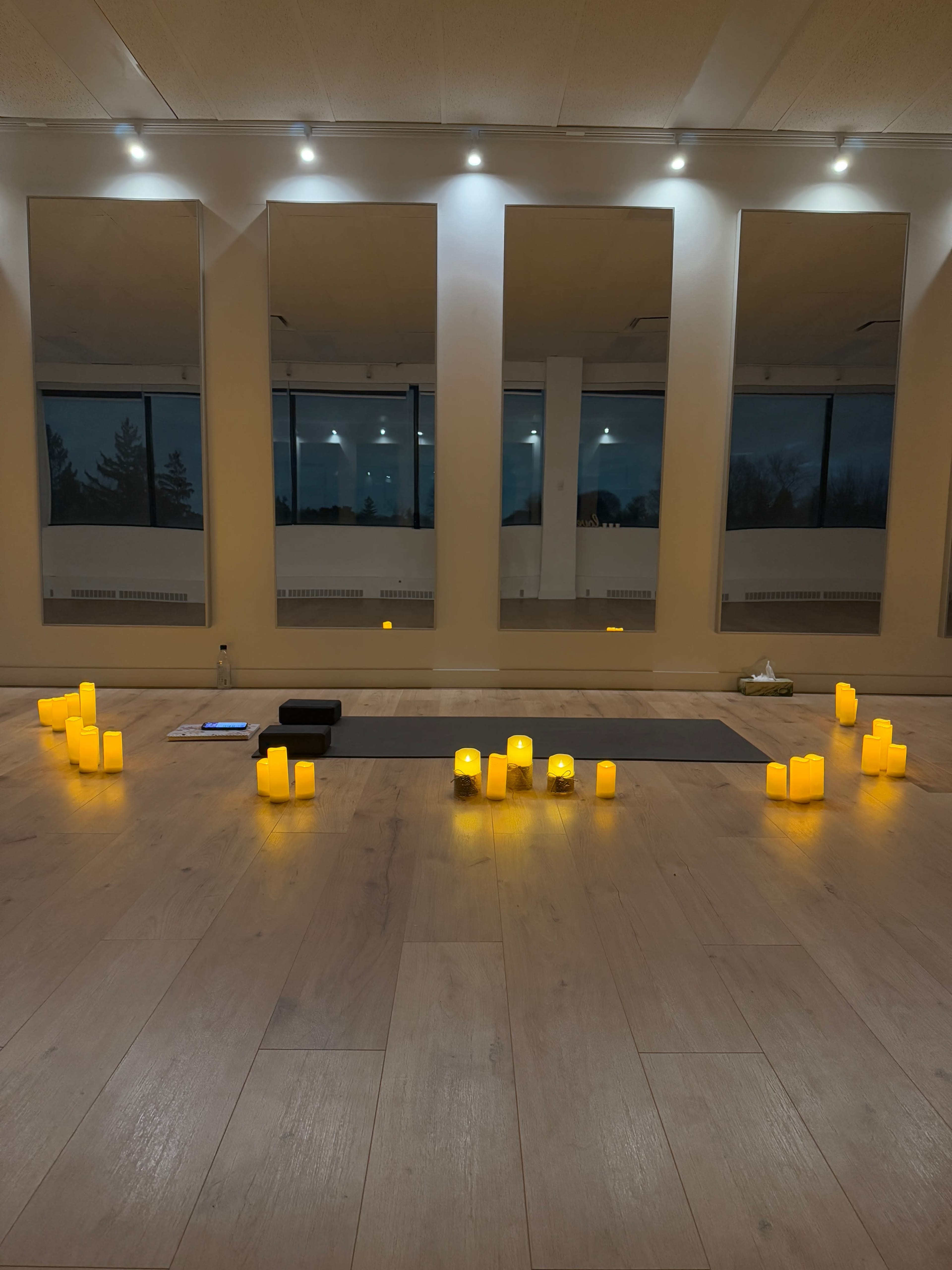 A meditation space is set up with flickering candles arranged around a yoga mat, and large mirrors reflecting the serene atmosphere.