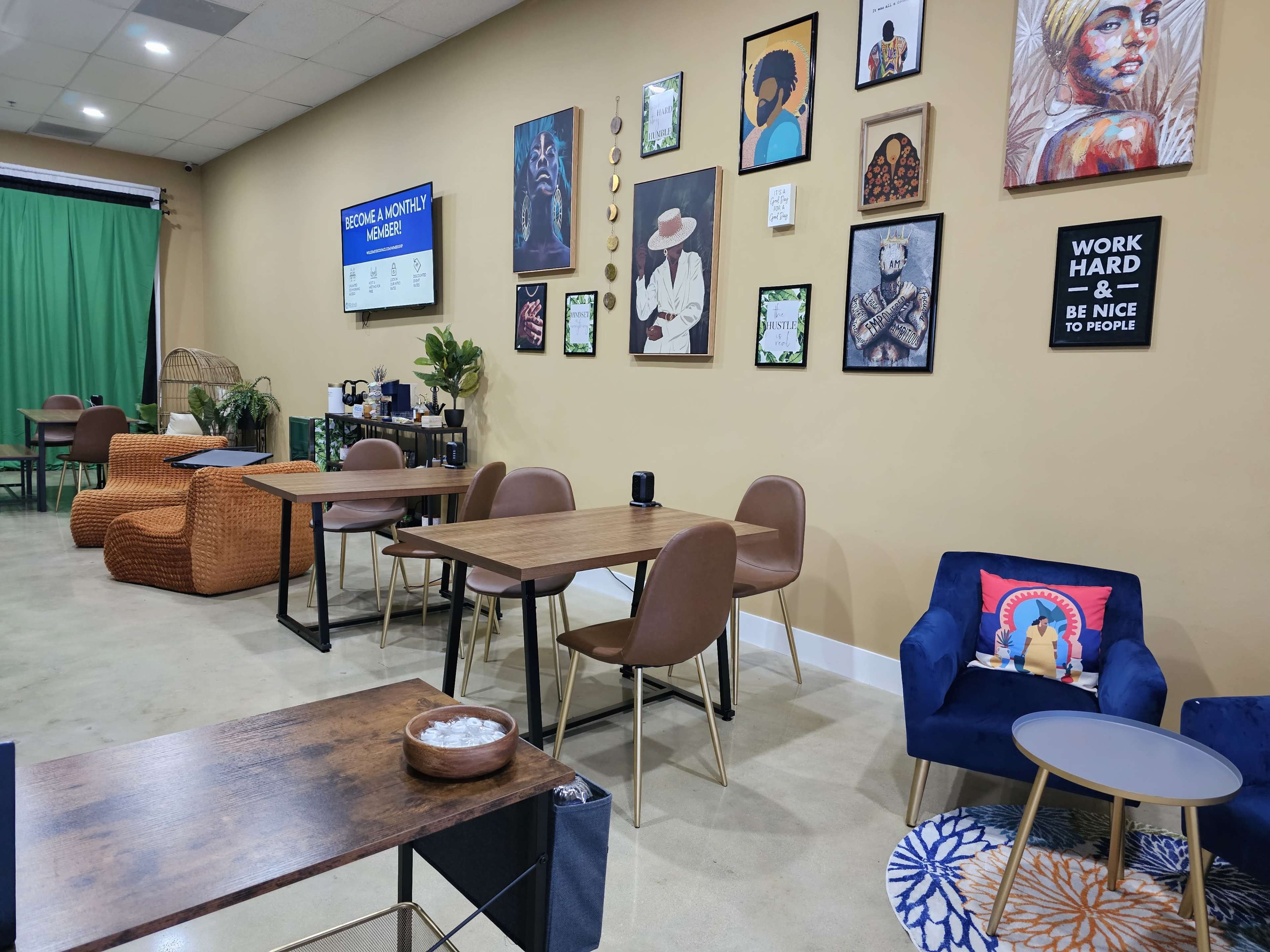 A cozy café interior with wooden tables, brown chairs, and wall art, featuring a green curtain and a small seating area with colorful cushions.