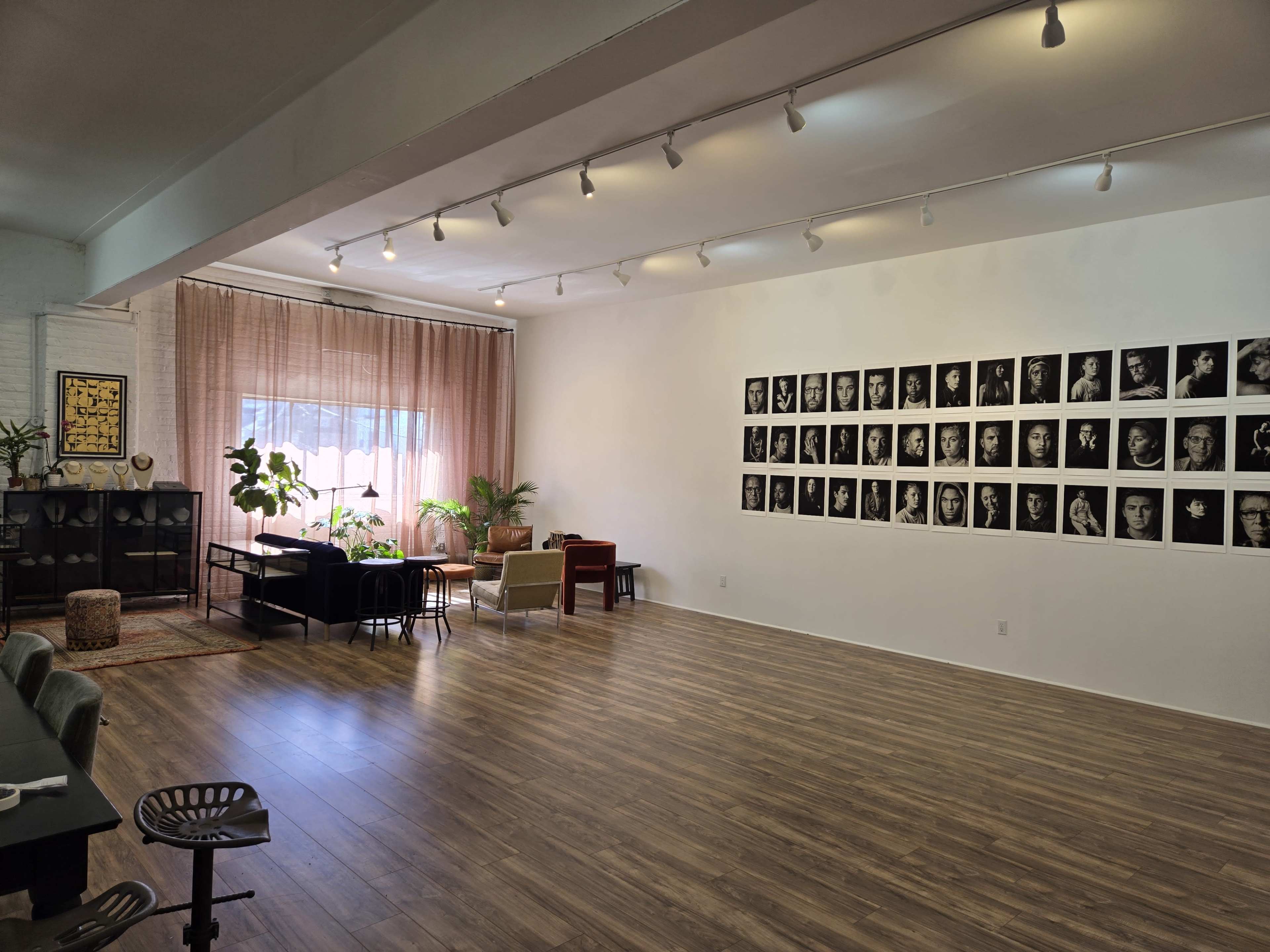 A spacious studio features a wall of black-and-white portraits, plants, and a mix of modern furniture arranged for a welcoming atmosphere.