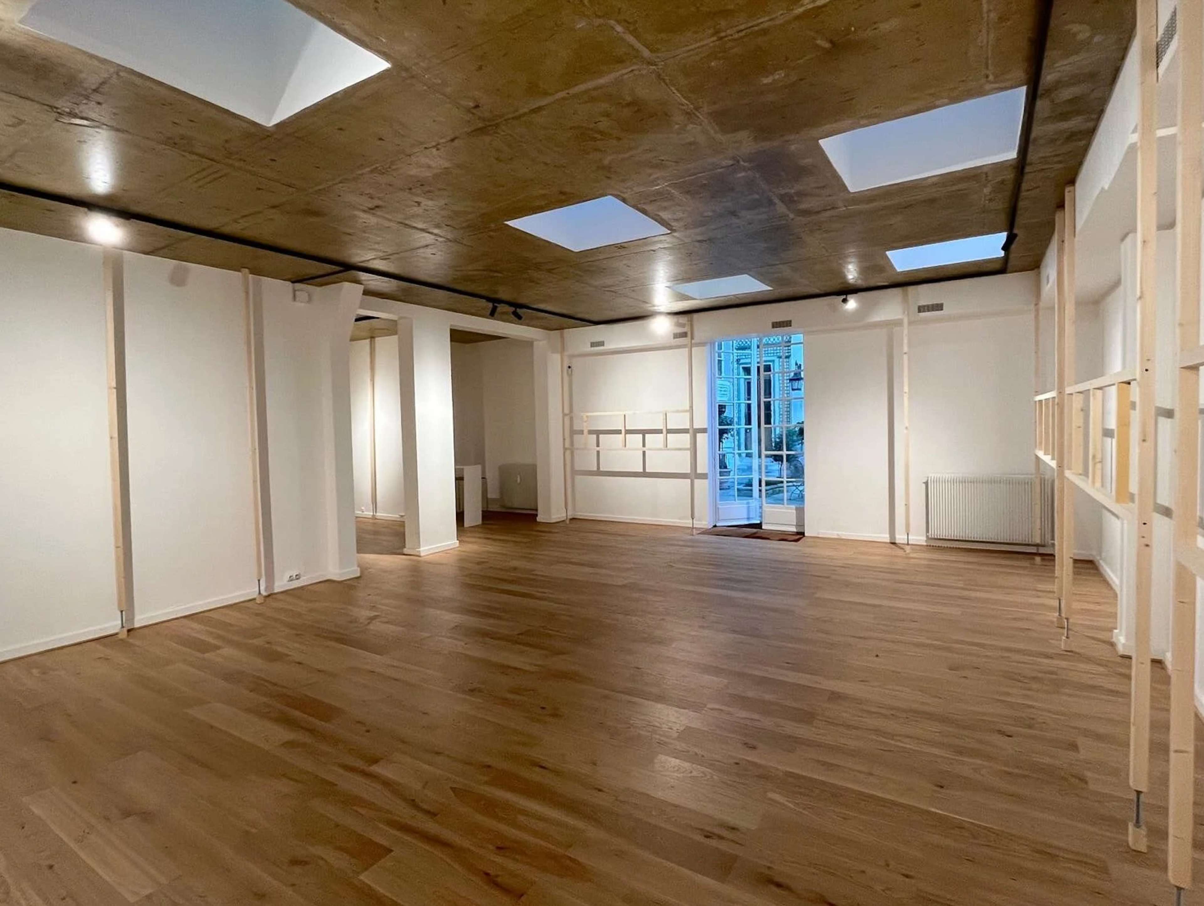 The image shows an empty, well-lit interior space with wooden flooring and skylights in the ceiling.