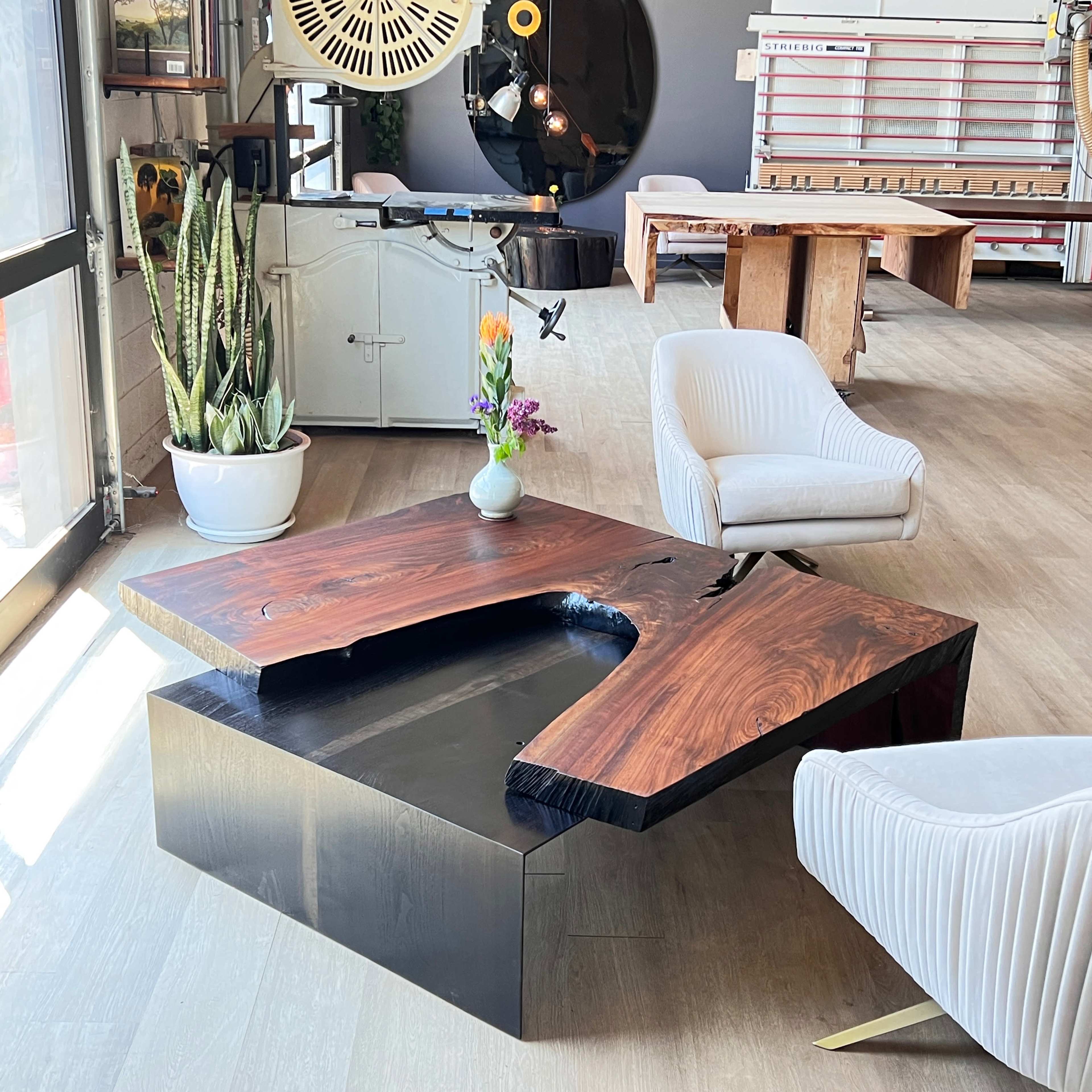 The image features a modern interior space with a unique wooden coffee table, a white armchair, and a vase of flowers, alongside various design elements and furniture pieces.