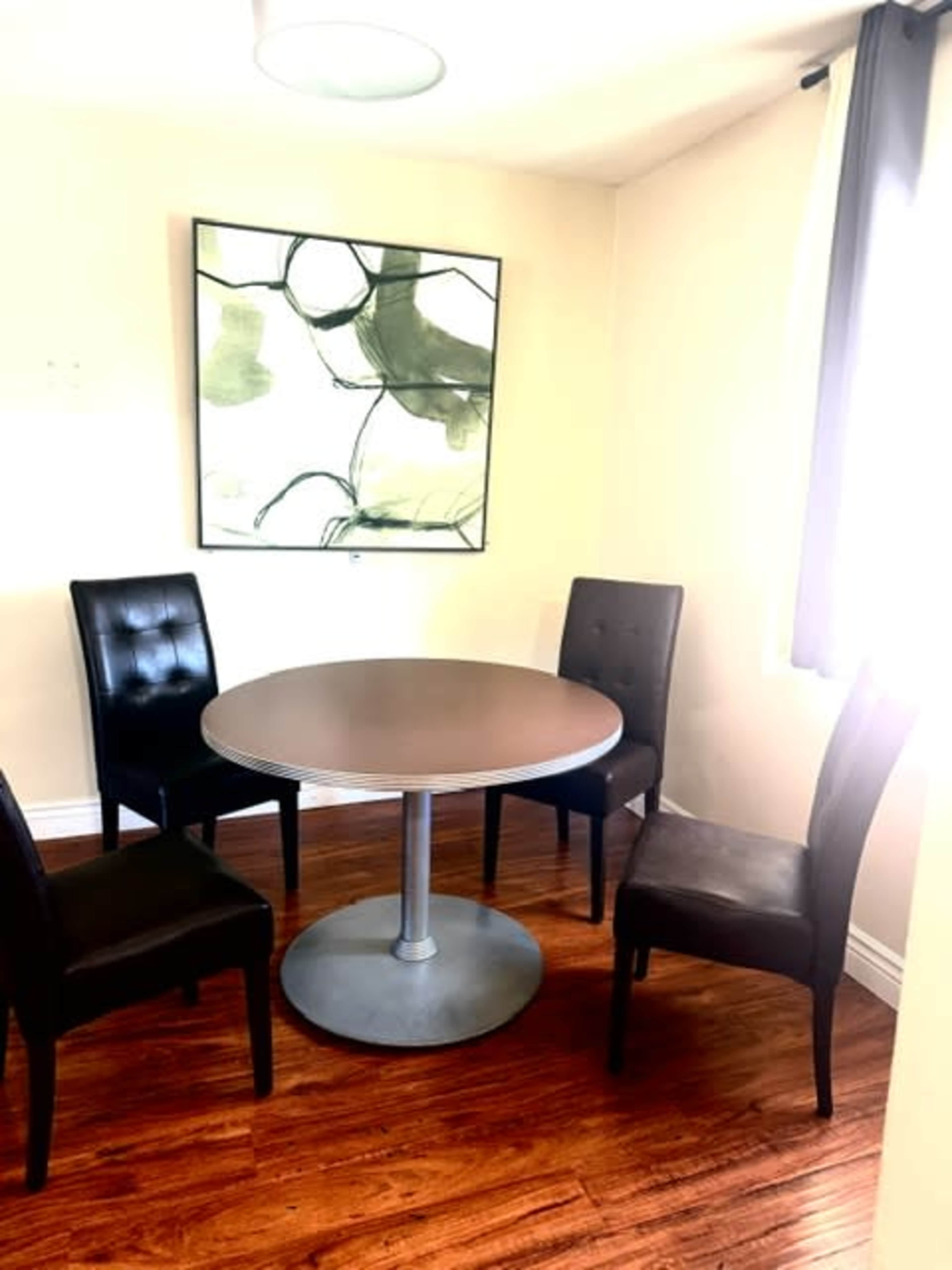 A round table with a metal base is surrounded by four black upholstered chairs in a well-lit dining area.