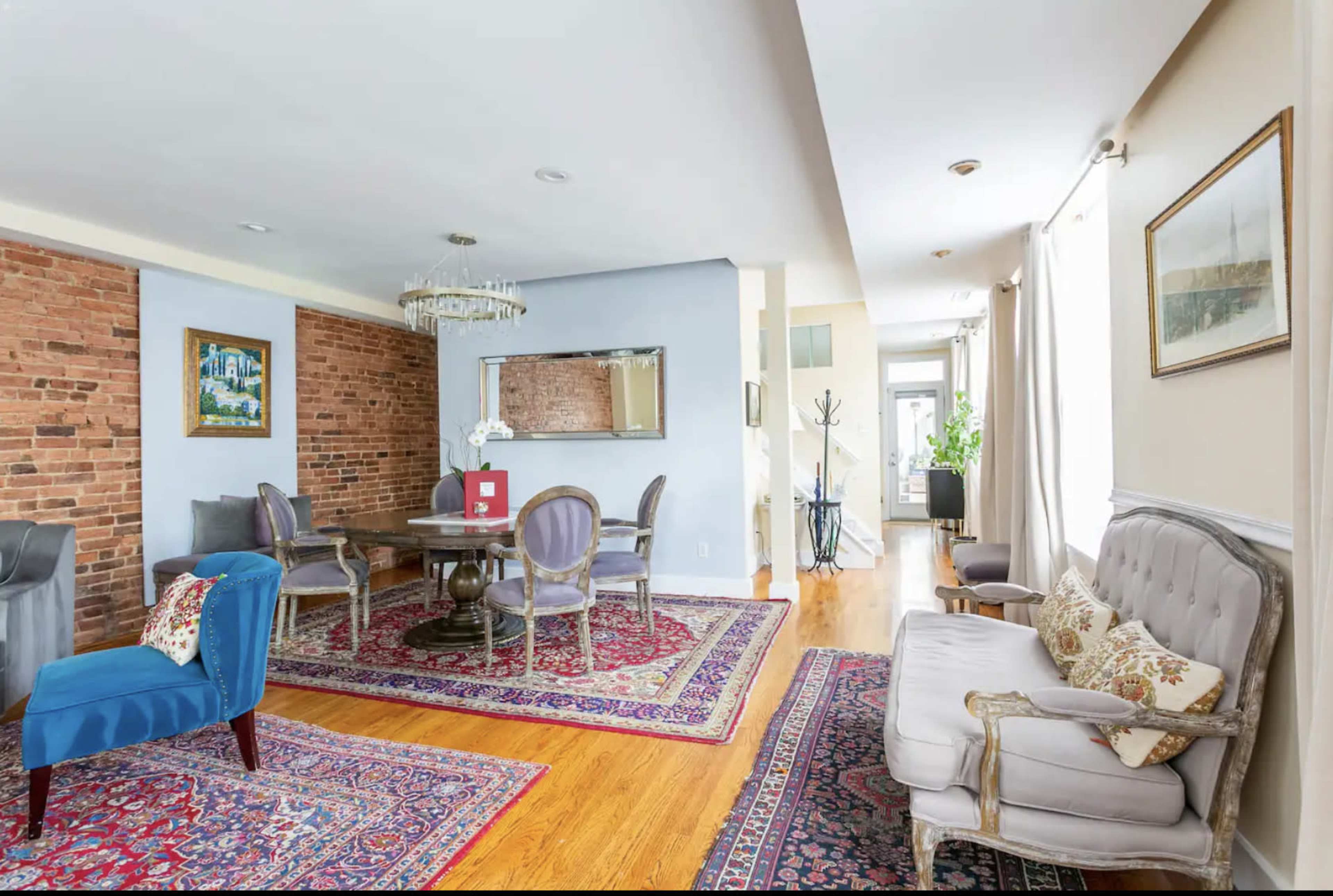 A spacious dining area with a round table surrounded by upholstered chairs, set against a backdrop of exposed brick walls and elegant rugs.