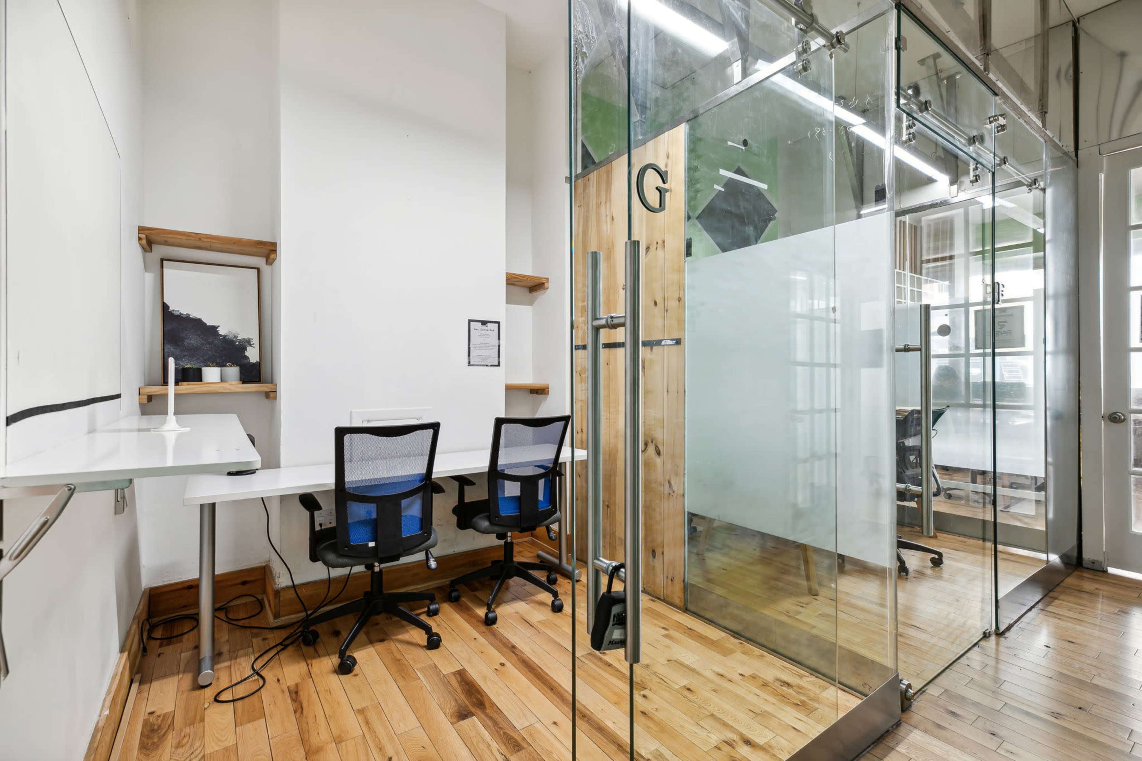 A modern office space featuring a glass meeting room and two black office chairs at a white desk.