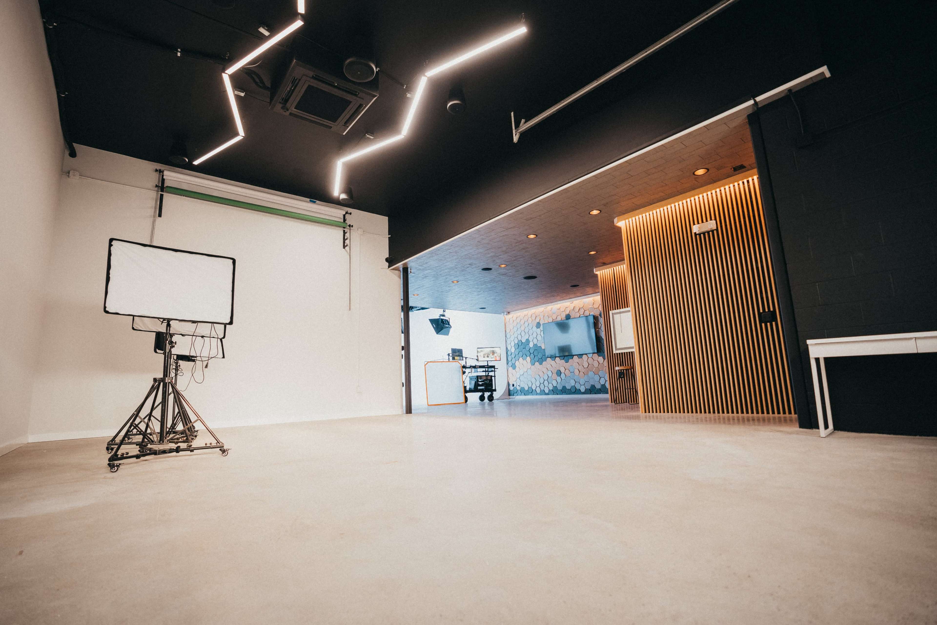A spacious, evenly lit studio featuring a lighting setup on a stand and a split design with one side having a black wall and the other side showing a patterned mural.