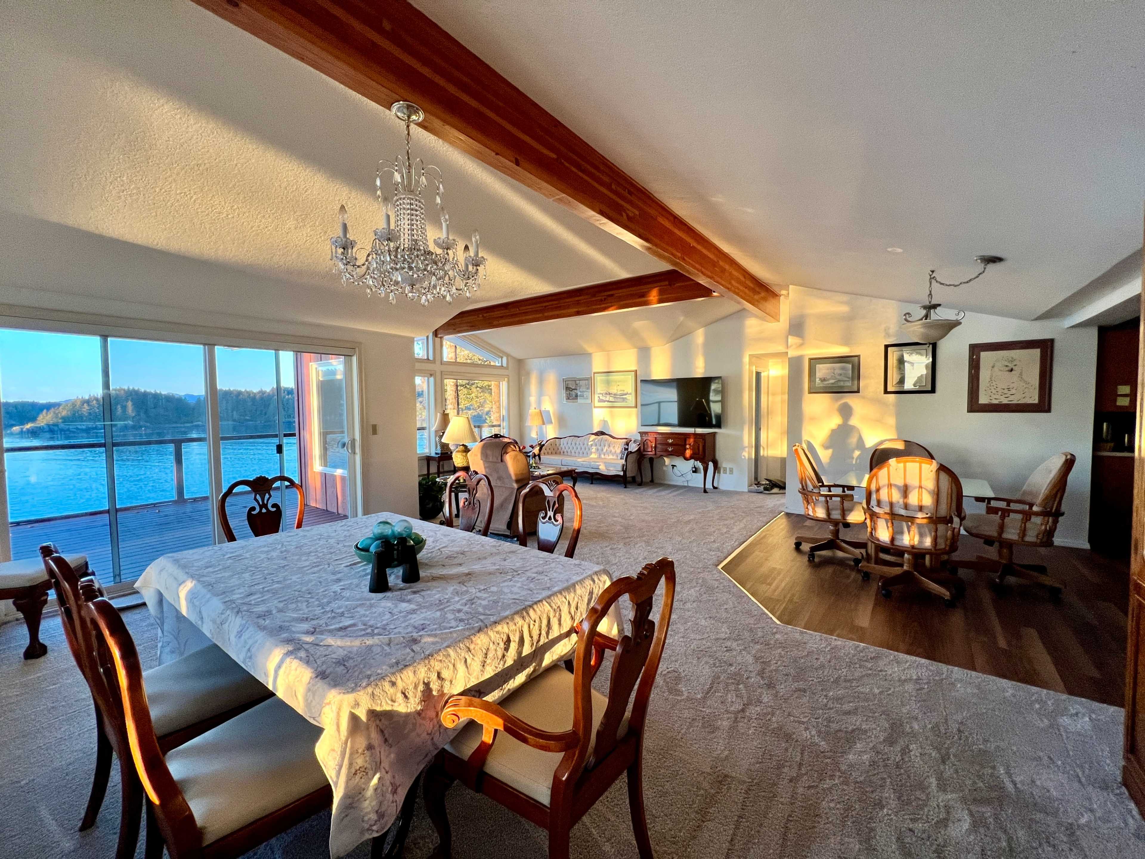 The scene features a well-lit dining area with a chandelier, a table set for dining, and a view of water through large windows.