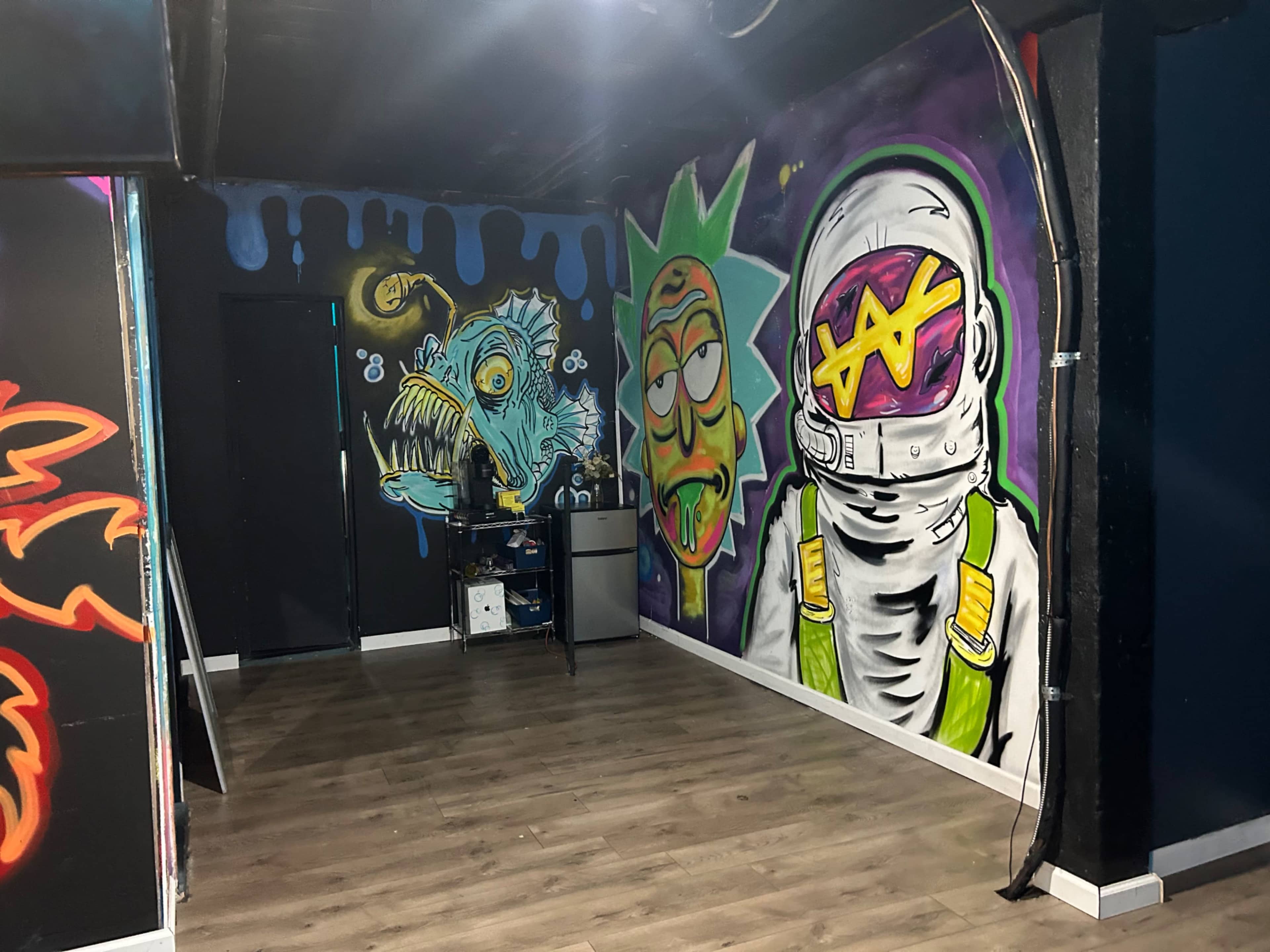A room with vibrant graffiti murals on the walls, depicting a cartoonish astronaut and a character resembling a green-haired figure, along with a stylized monster, in front of a dark backdrop.