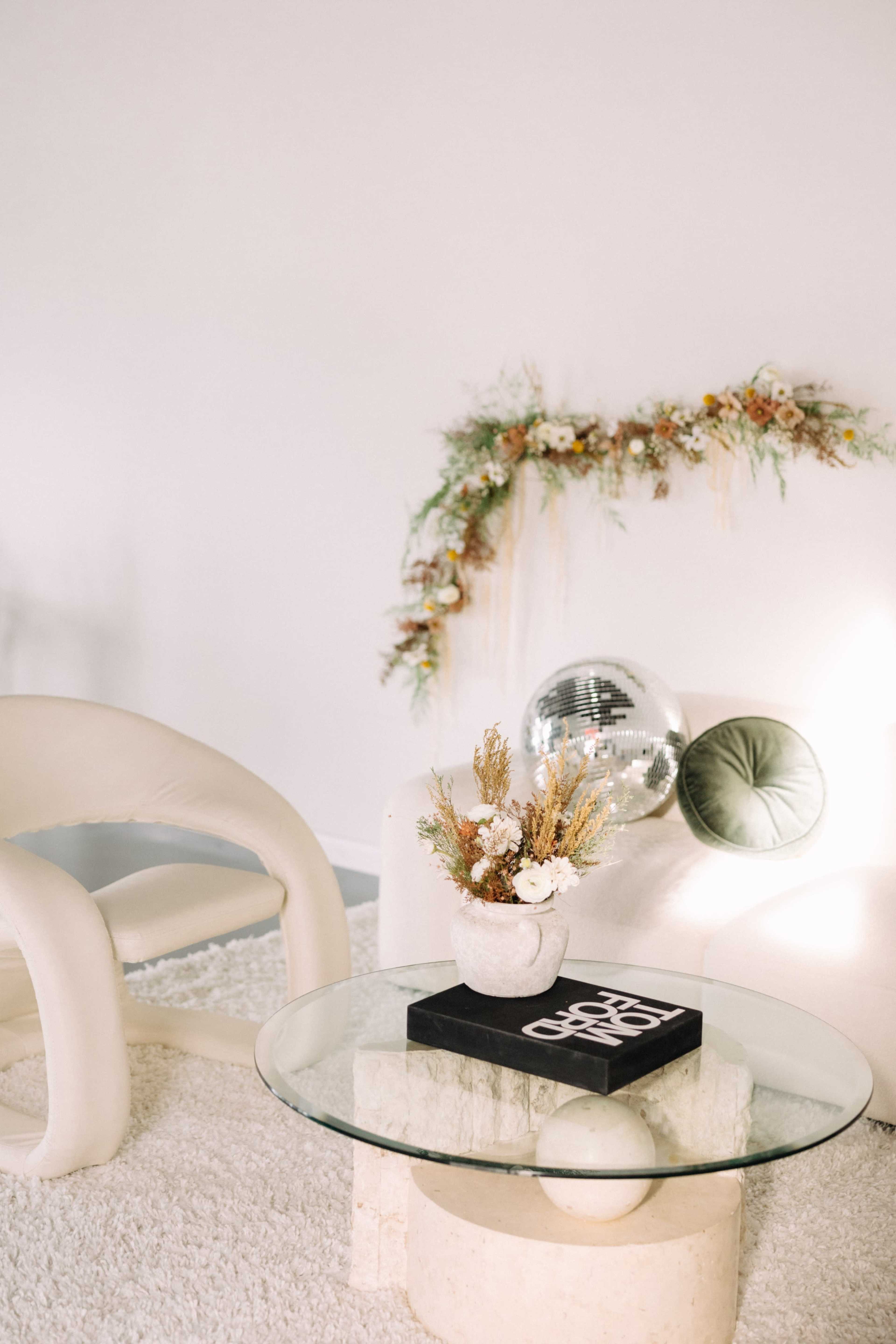 A minimalist living room scene features a glass coffee table with a decorative vase and a disco ball, surrounded by a plush rug and modern furniture.