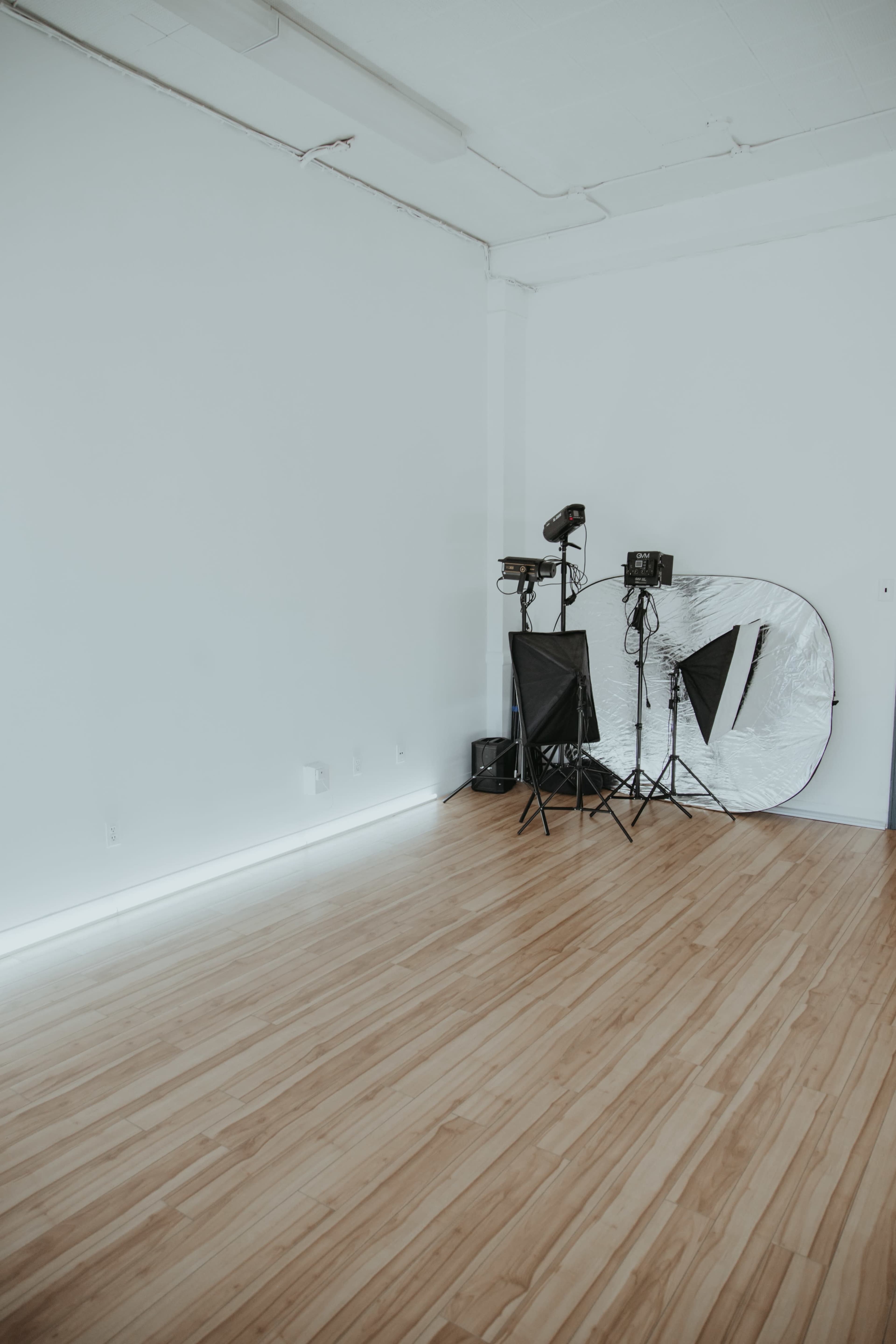 A minimalistic studio space with wooden flooring, white walls, and photography equipment set up in one corner.