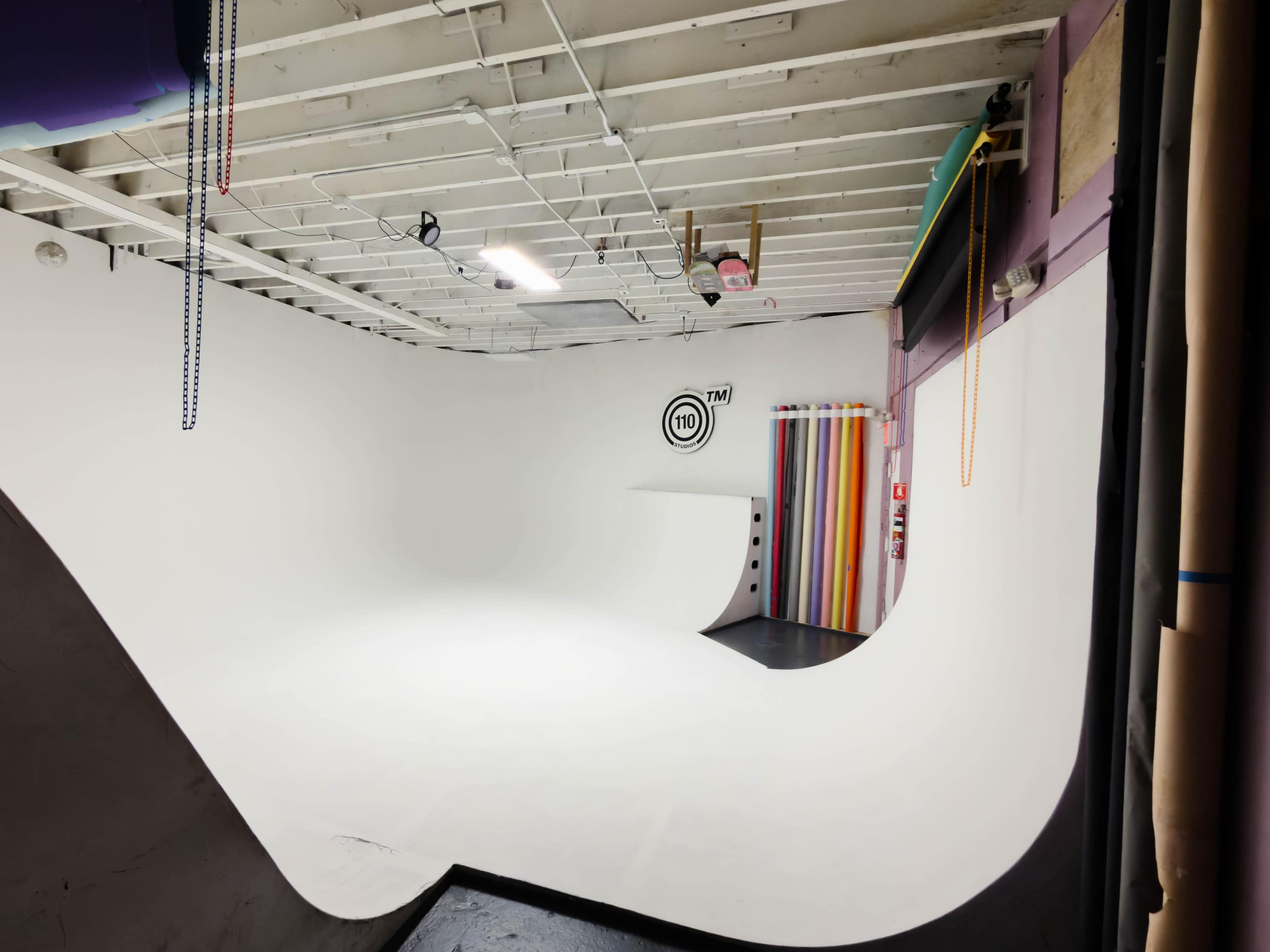 The image shows a spacious photo studio with a seamless white backdrop and colorful drapes on one side.