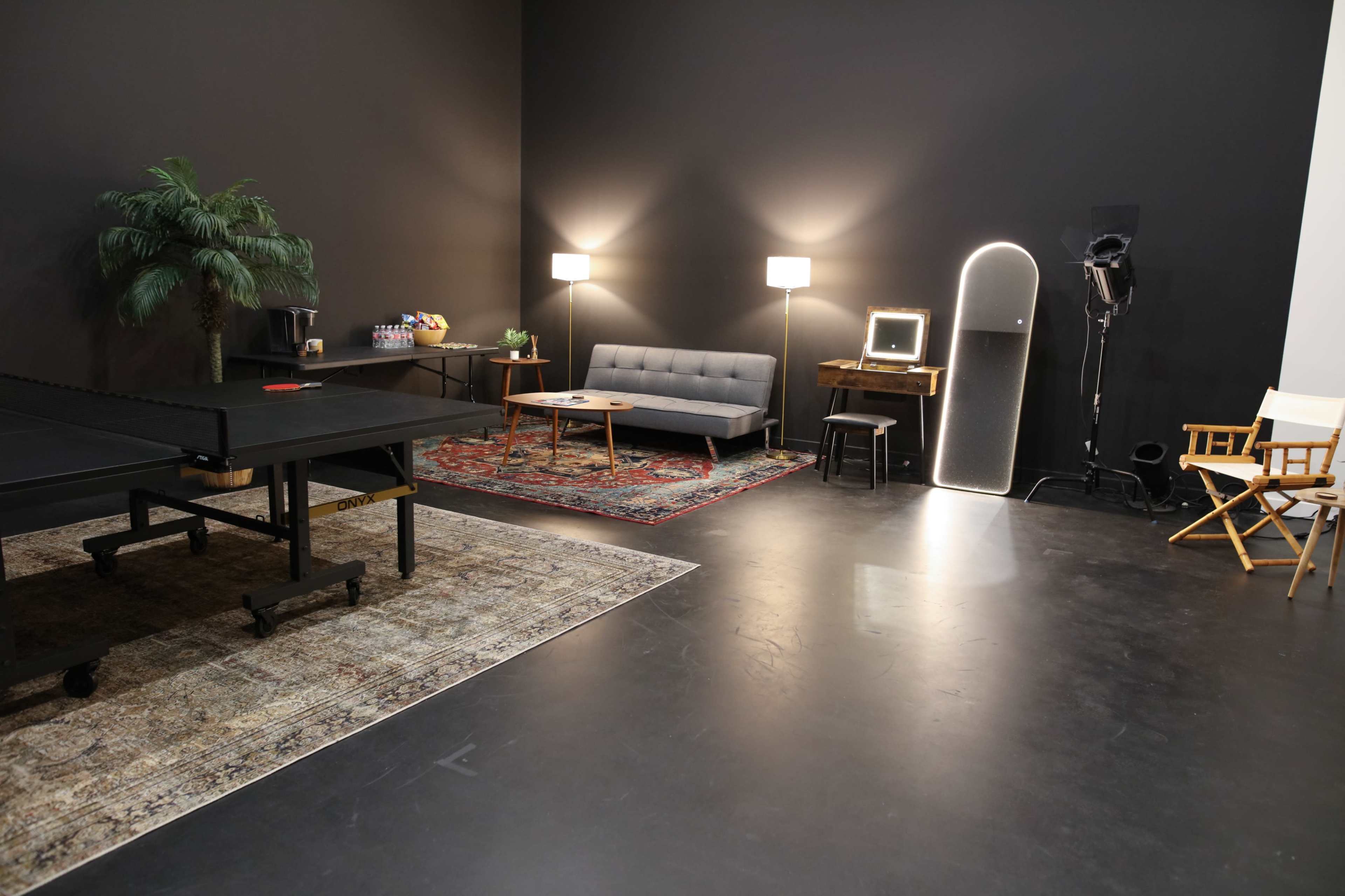 The image shows a modern studio space with a ping pong table, a sofa, and various light sources against a dark wall.