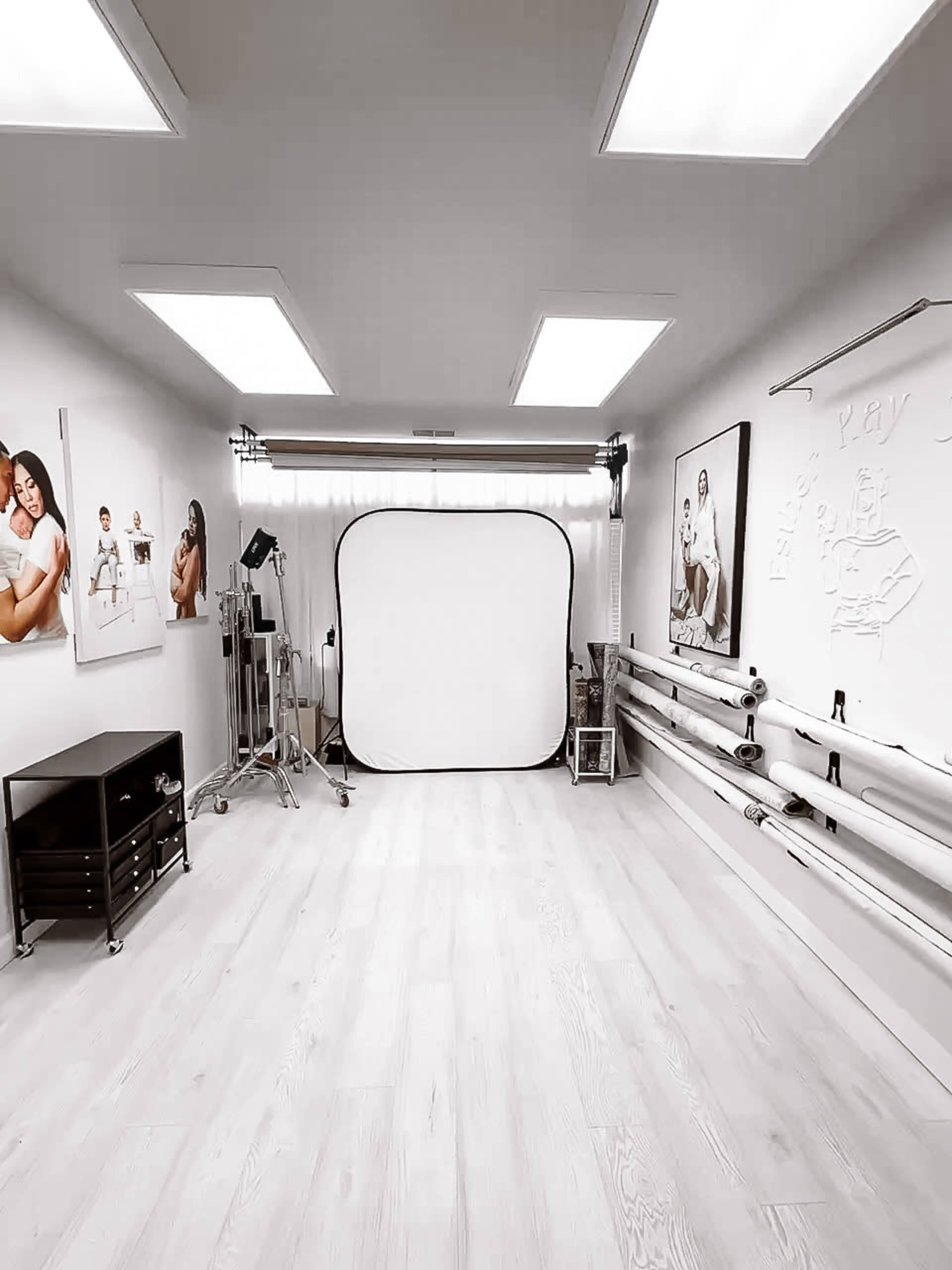 The image shows a photography studio with a large backdrop, lighting equipment, and various rolls of materials along the wall.