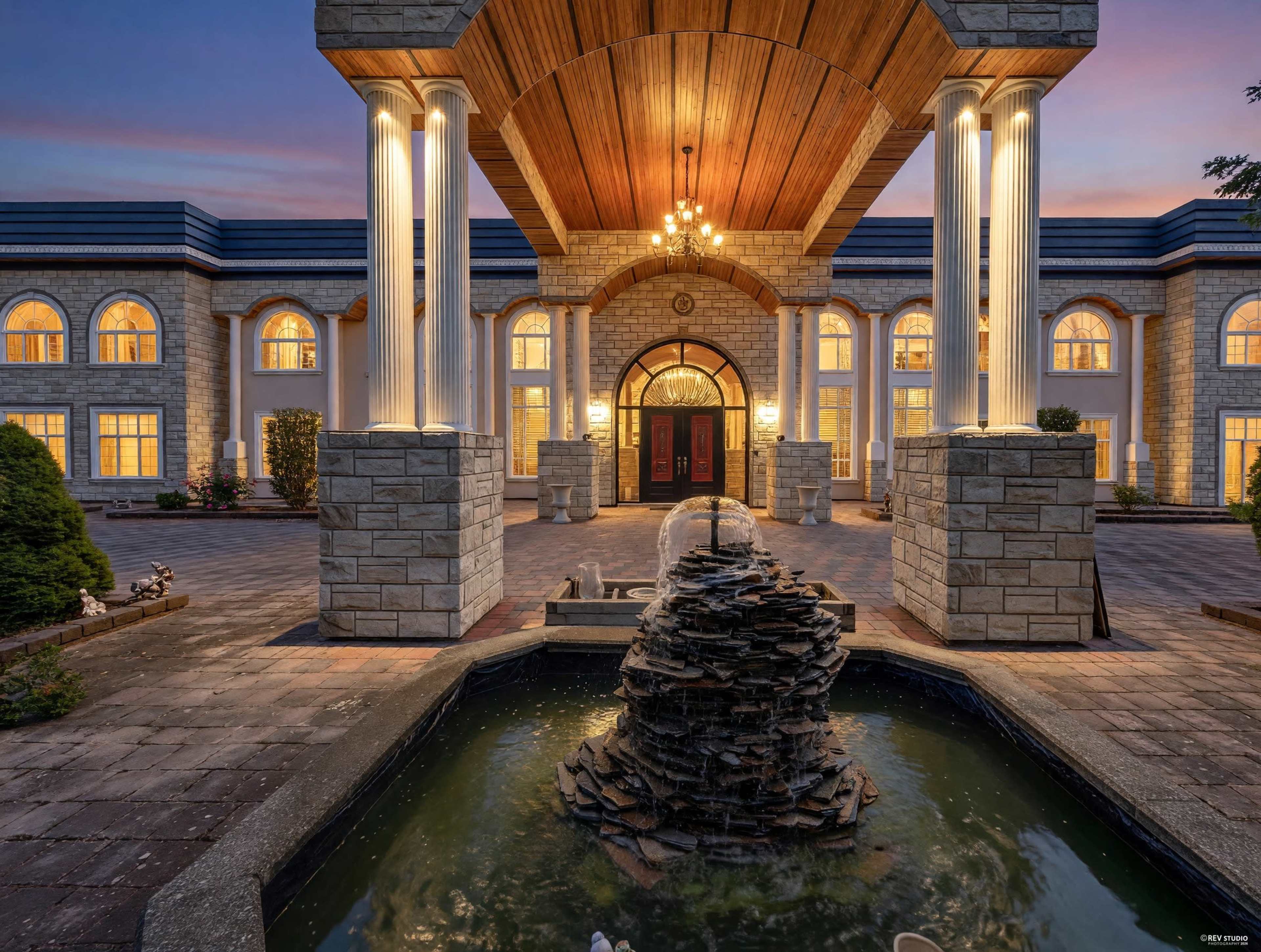 A grand entrance featuring a stone façade, a large overhang with a chandelier, and a fountain in a reflective pool.