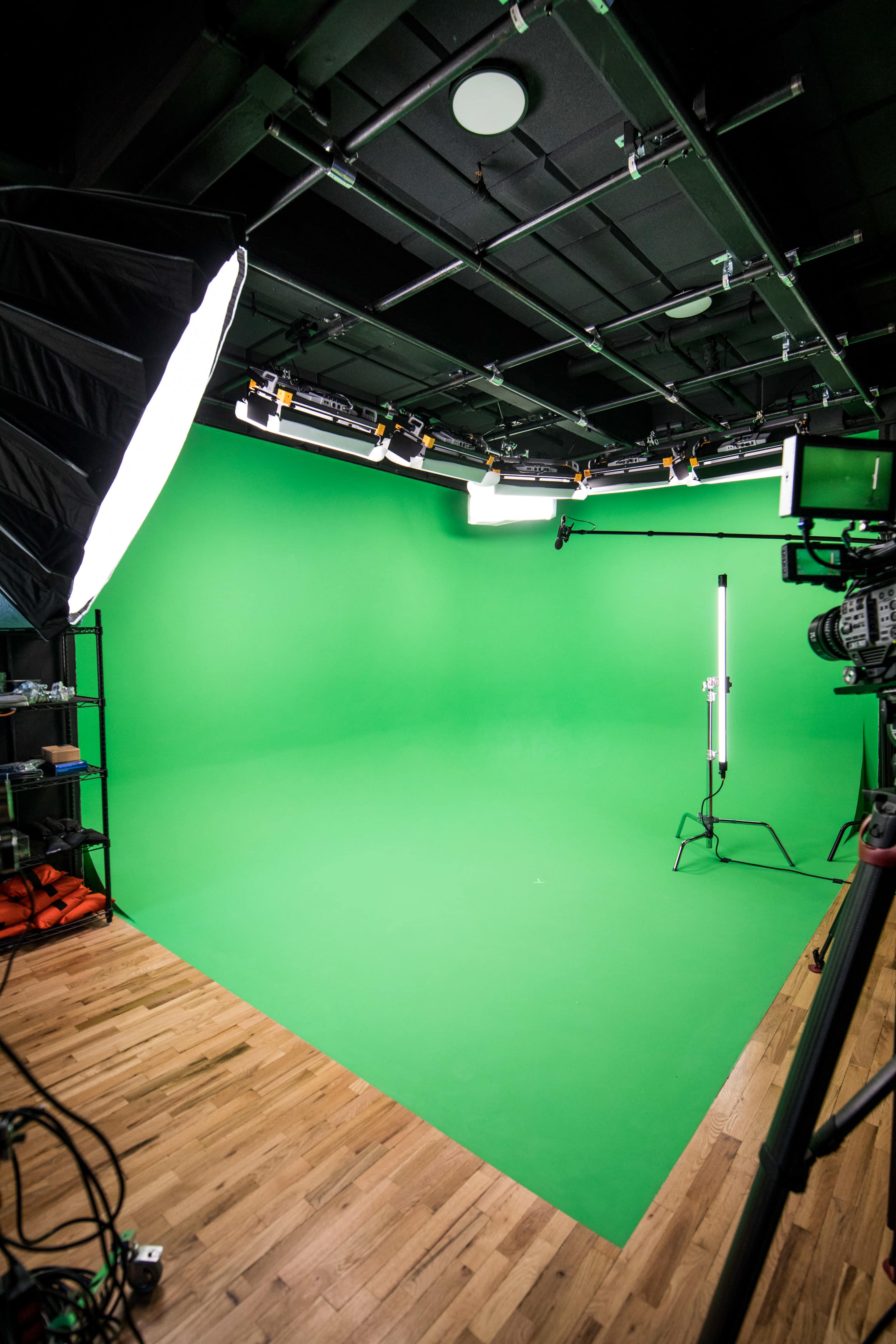 A green screen studio with overhead lighting and a wooden floor.