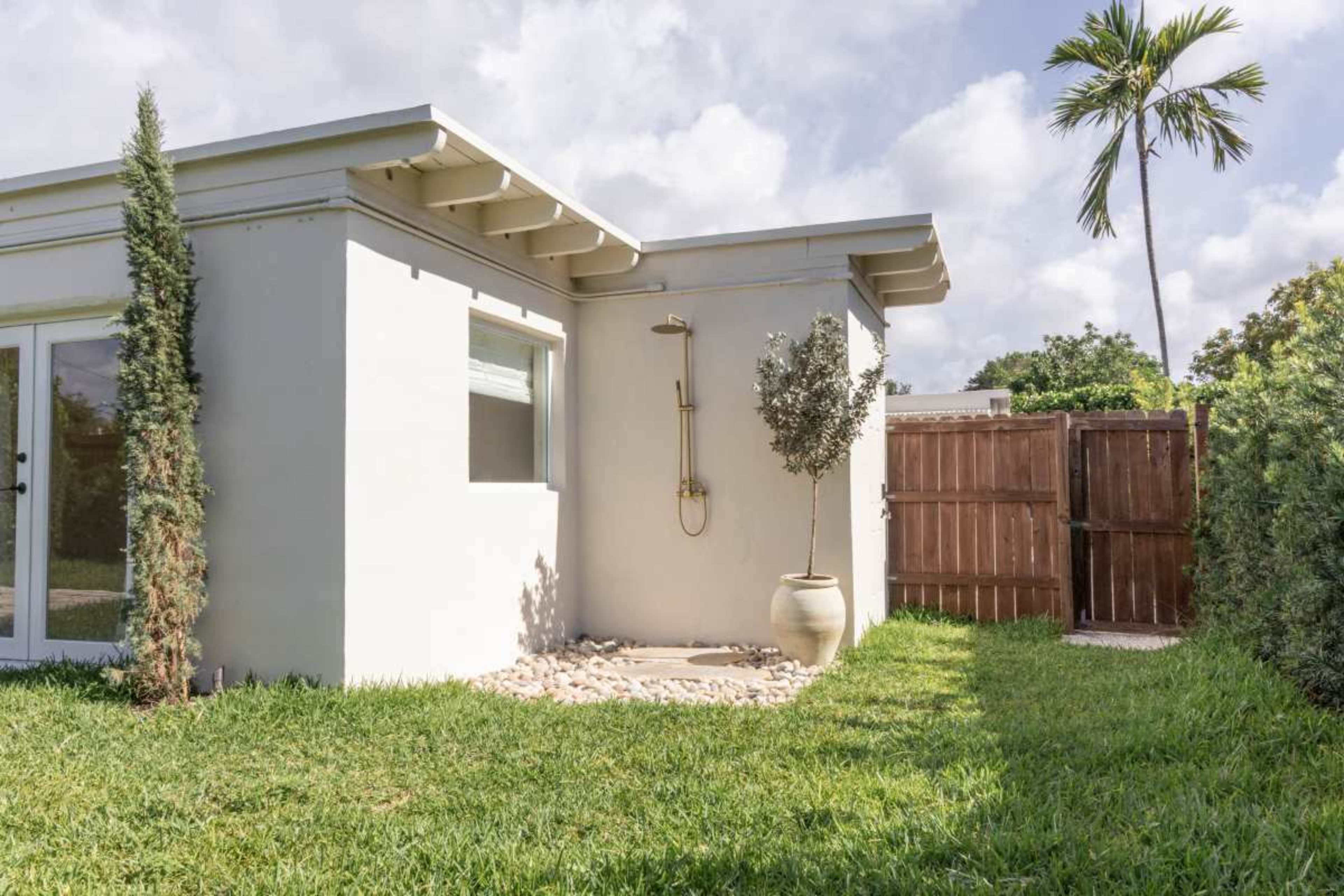 A modern house exterior features a corner shower and a decorative plant beside a wooden fence.